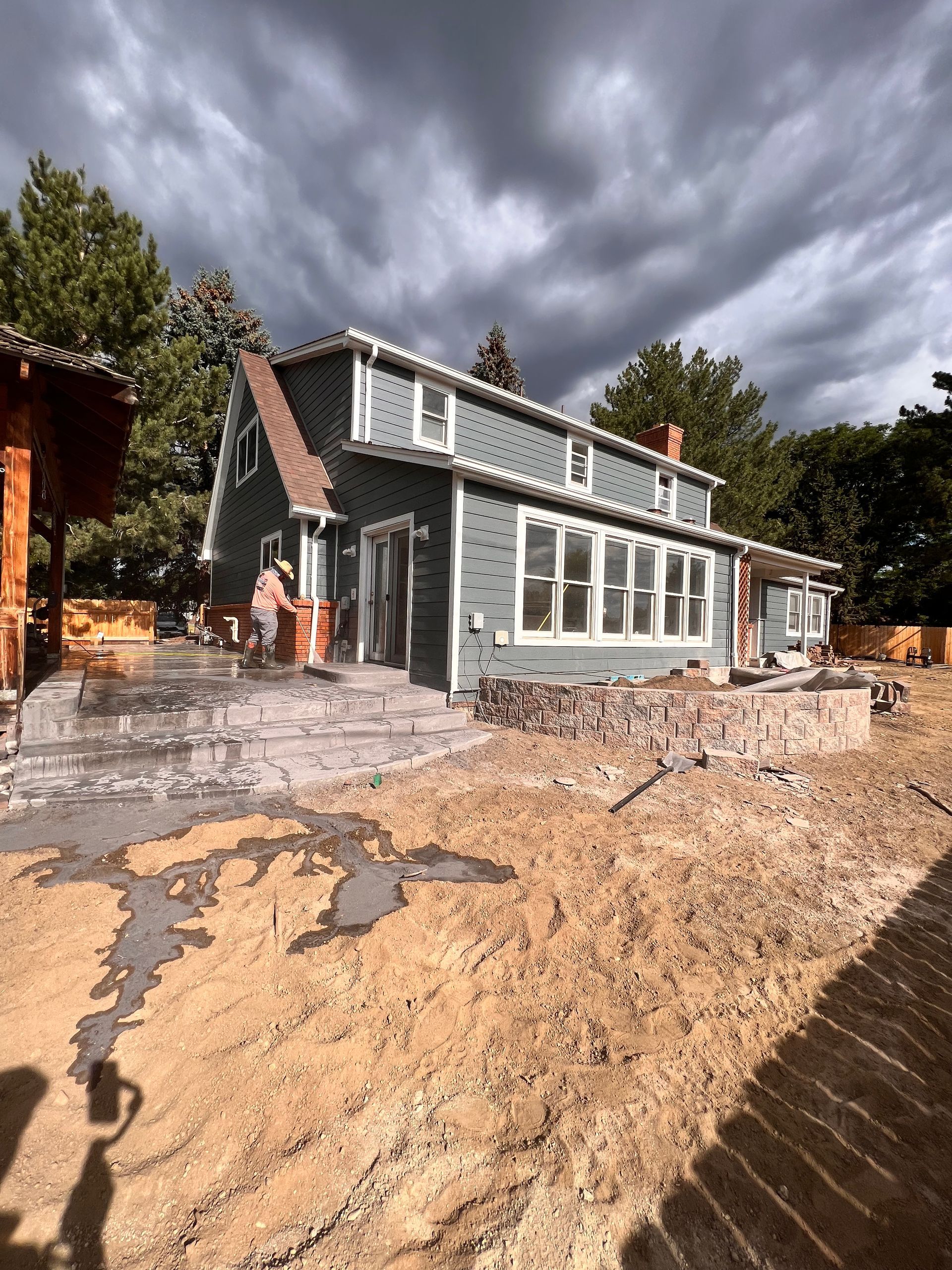 House exterior under construction, light blue siding, gray patio, person working on patio under stormy sky.