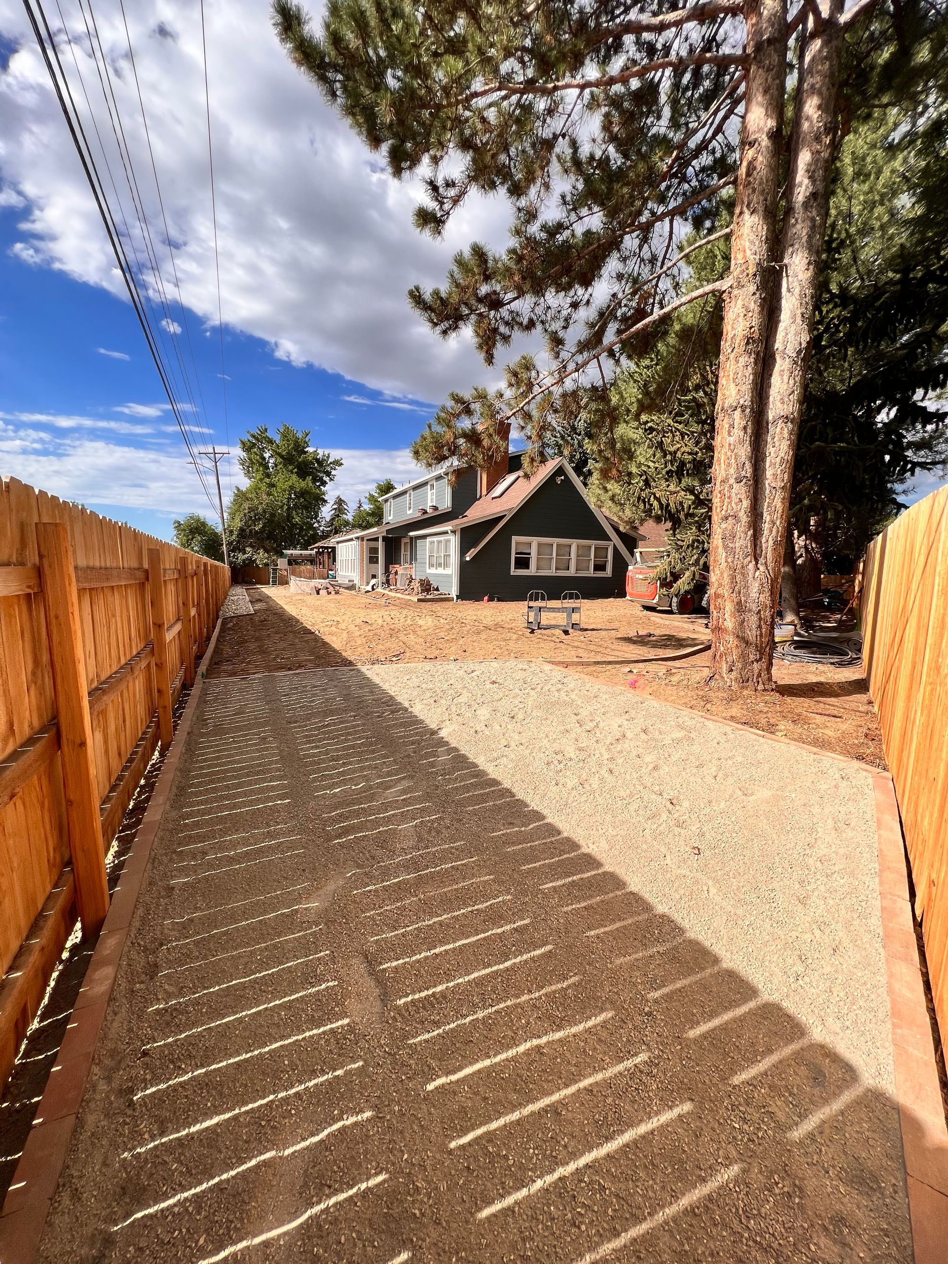Gravel driveway leading to a green house, fenced on both sides, under a blue sky.