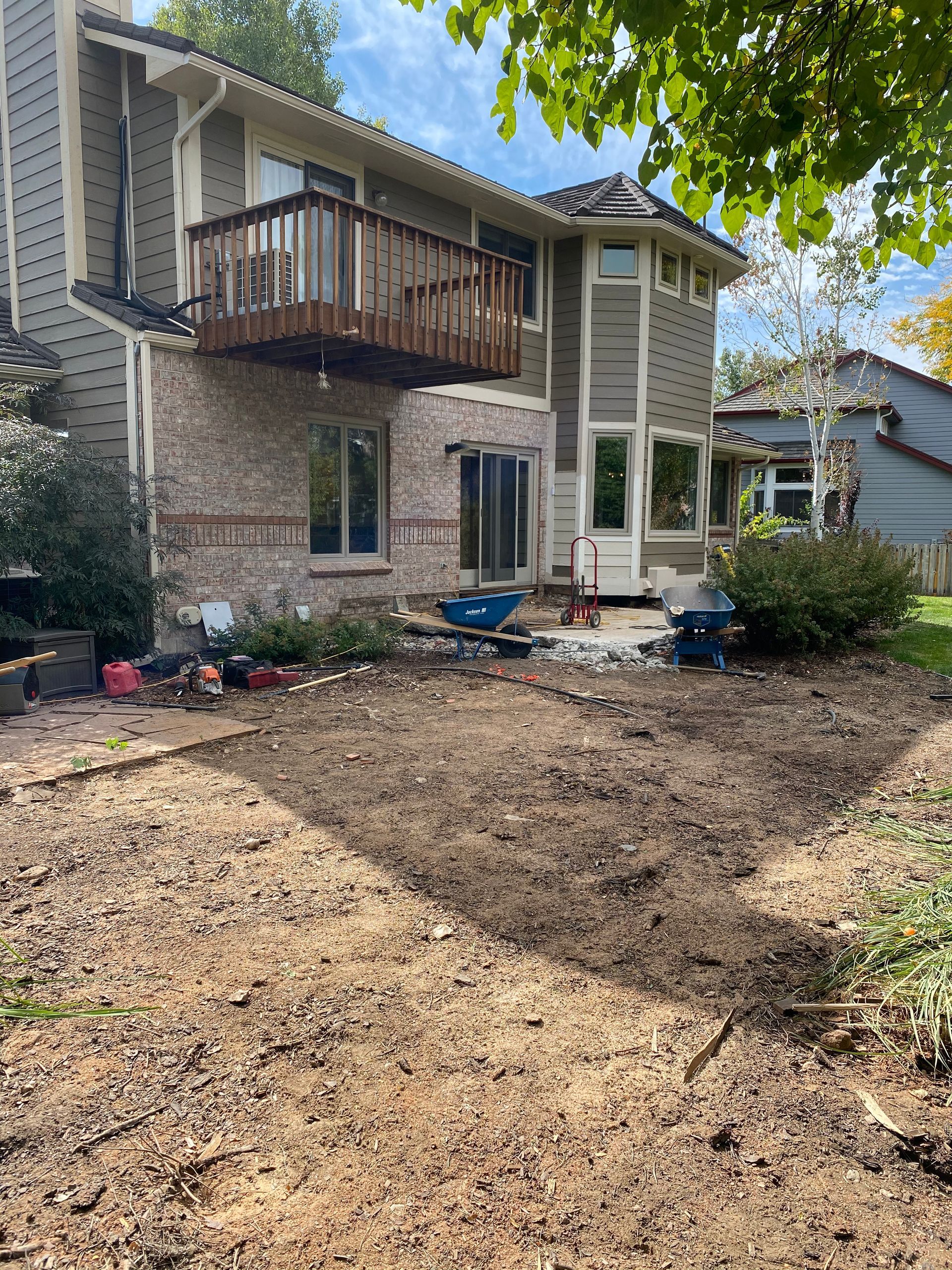 Backyard with a two-story house, deck, and exposed dirt; construction materials scattered.