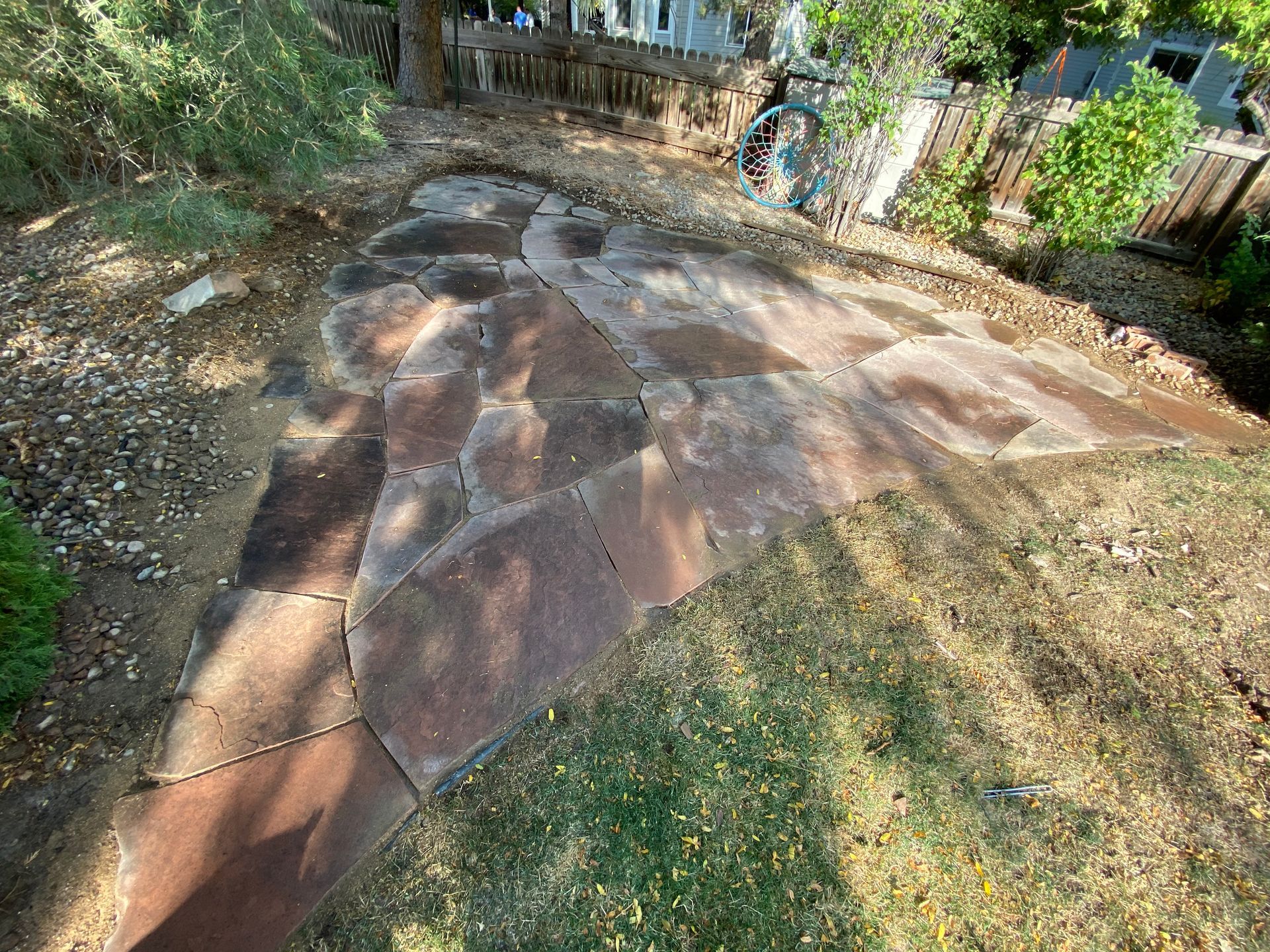 Flagstone patio with a pathway surrounded by grass and dirt.