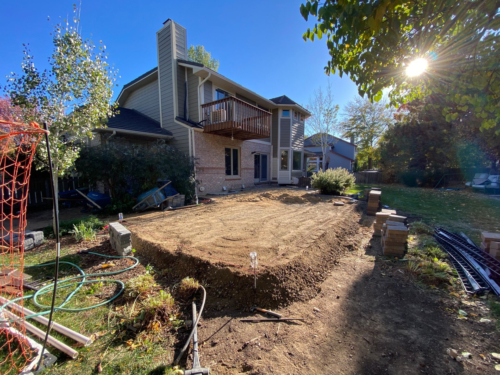 Backyard excavation in progress; brick house with balcony and chimney in background.