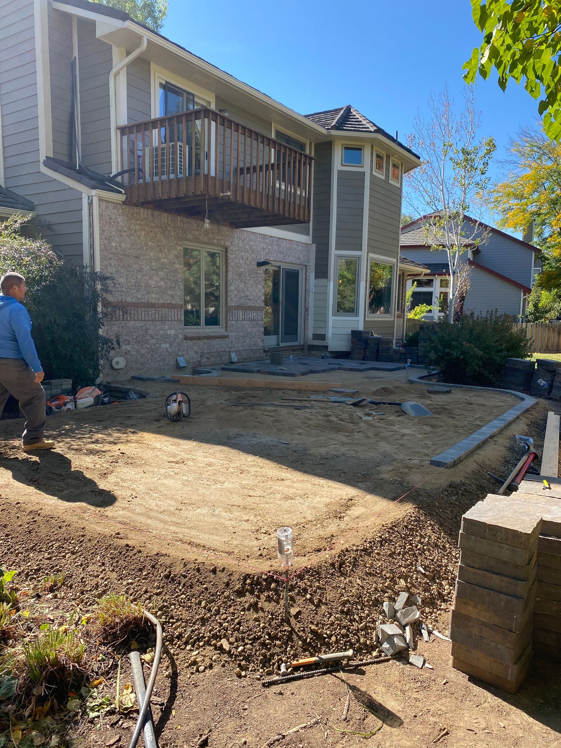Backyard construction: man near house with deck, exposed dirt, and landscaping materials.