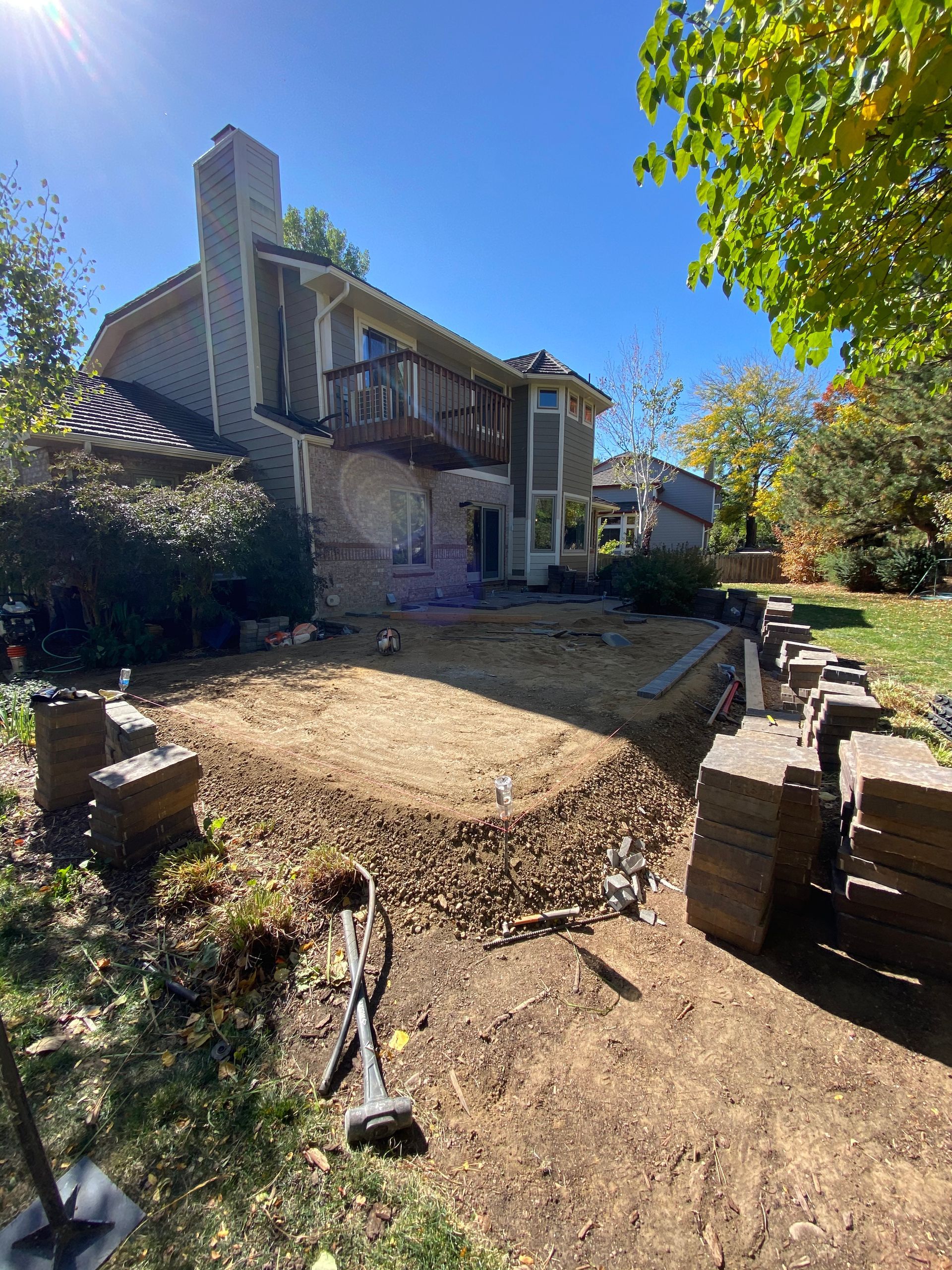 Backyard construction. A house with a balcony in the background. Gravel and building materials in the foreground.
