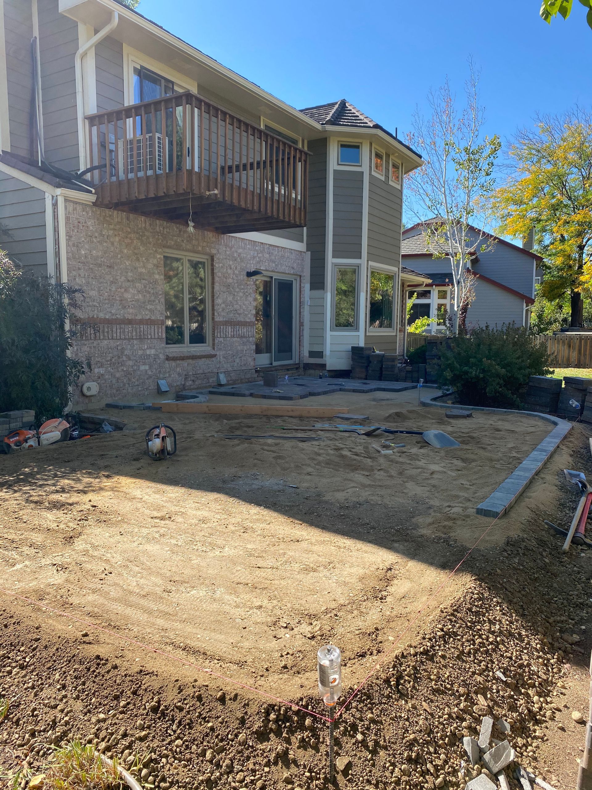 Backyard undergoing construction with dirt, pavers, and a house with a balcony.