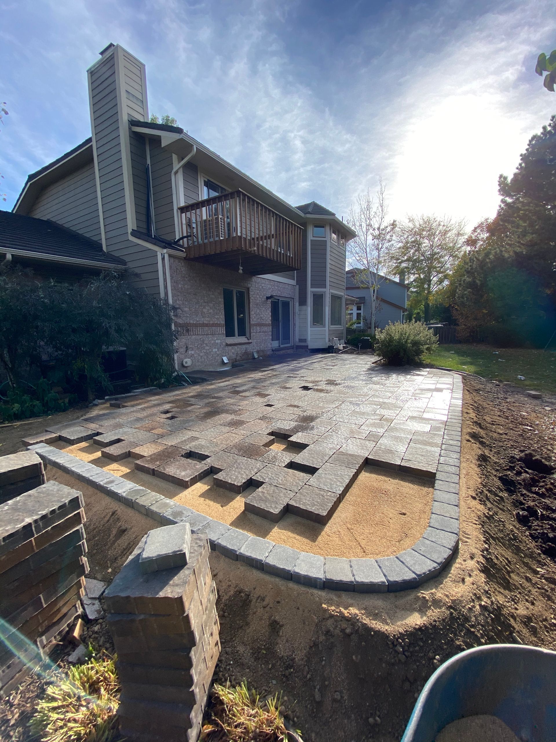Backyard patio construction with brickwork, beige sand, and house with a deck.