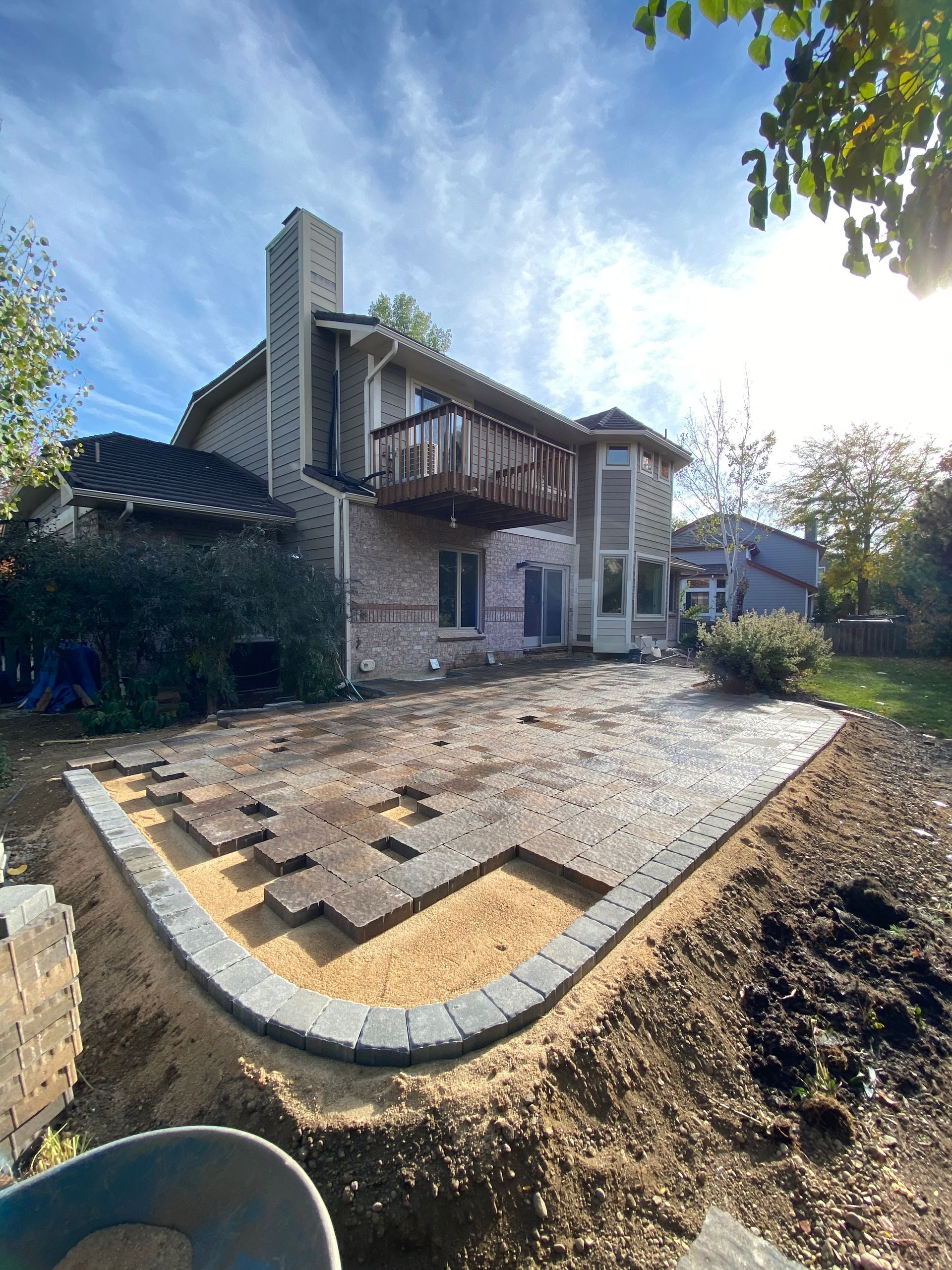 Backyard patio under construction with house in background, retaining wall, and pavers.