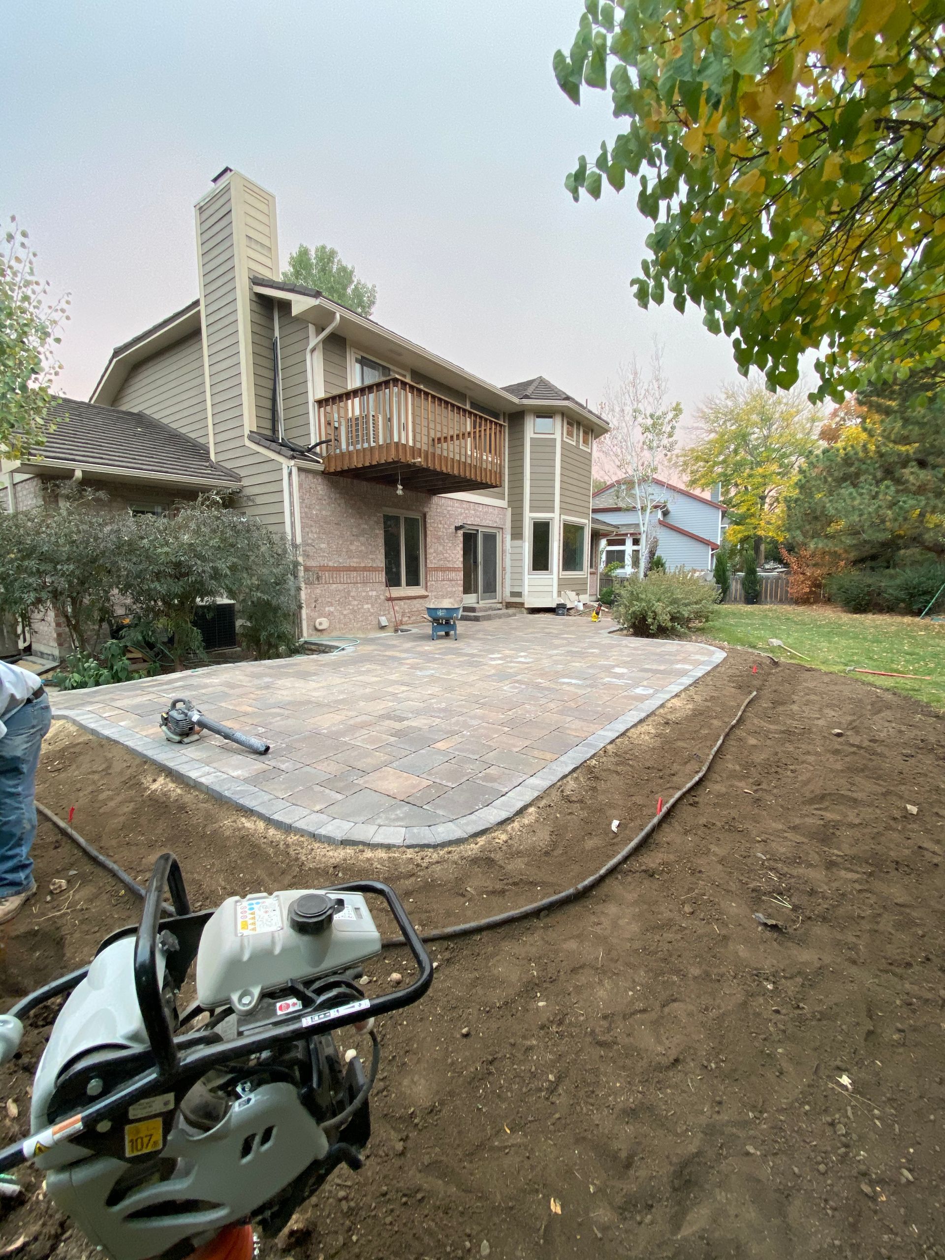 Backyard patio construction, house in background, with compactor, dirt, and new pavers.