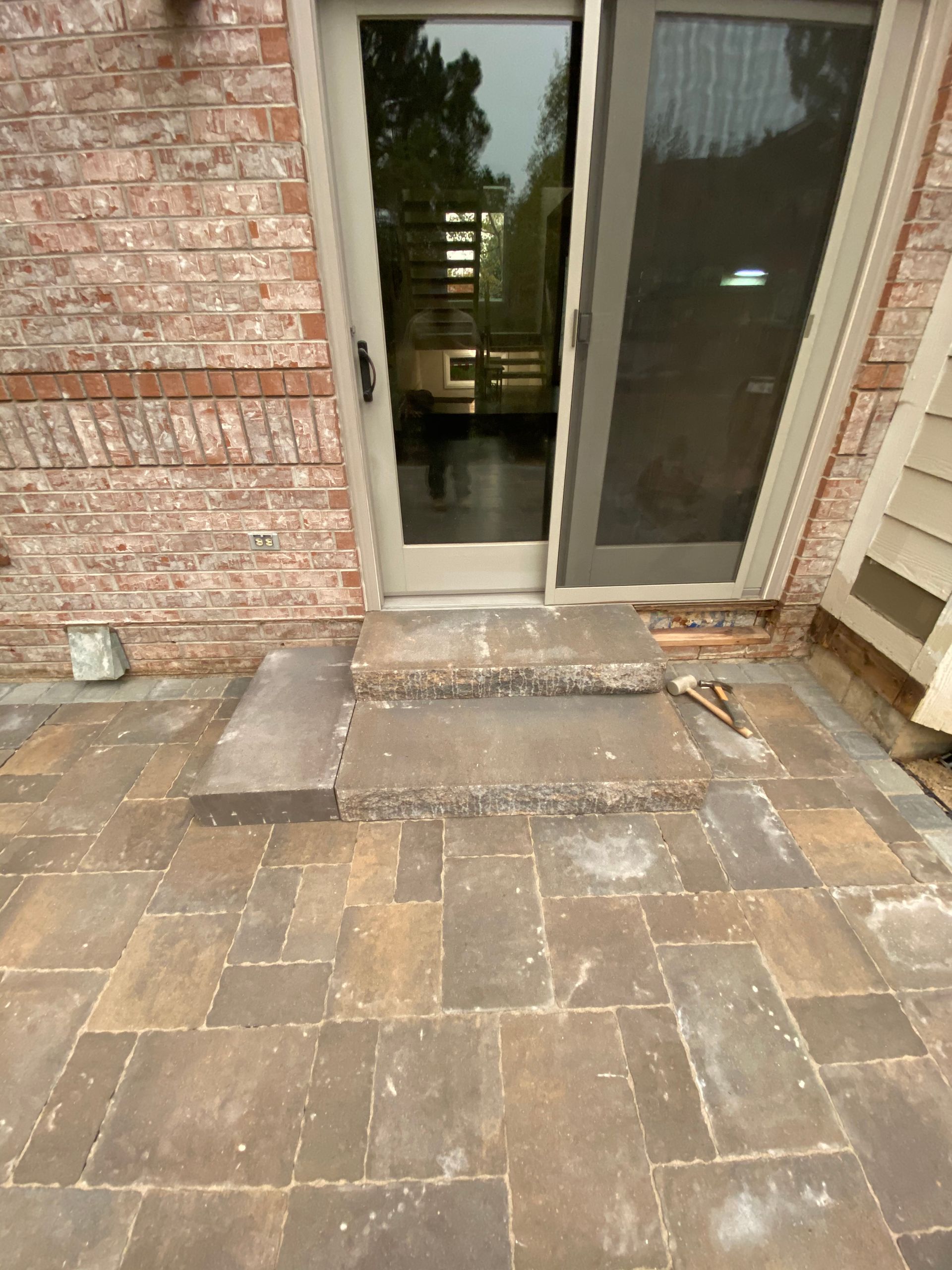 Brick patio with two steps leading to a glass sliding door.