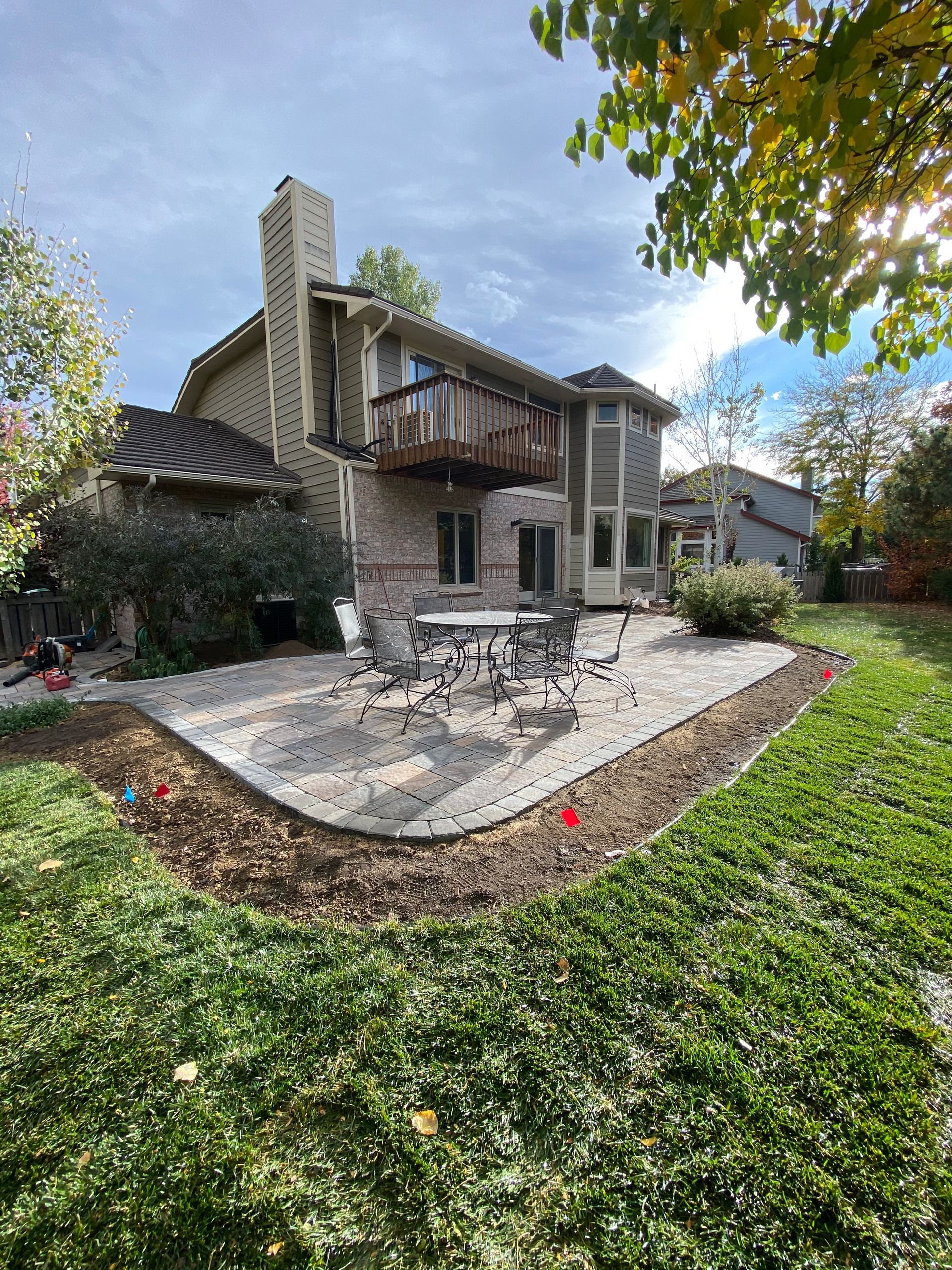 Backyard patio with brick house, seating, and green lawn on a sunny day.