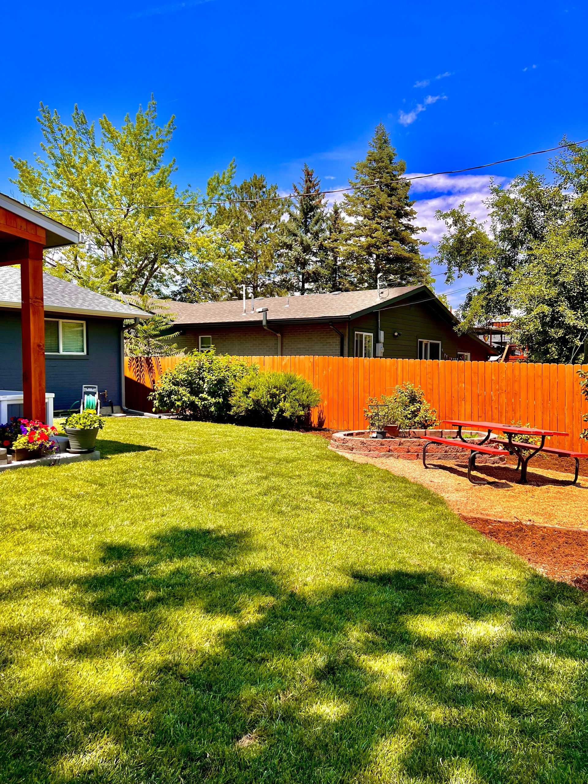 Backyard with green lawn, orange fence, picnic table, and blue sky.
