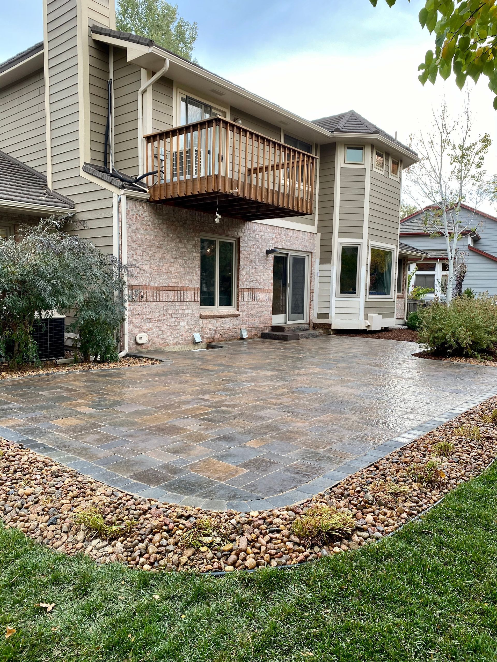 Back patio with brick house, balcony, stone pavers, rock border, and grass.