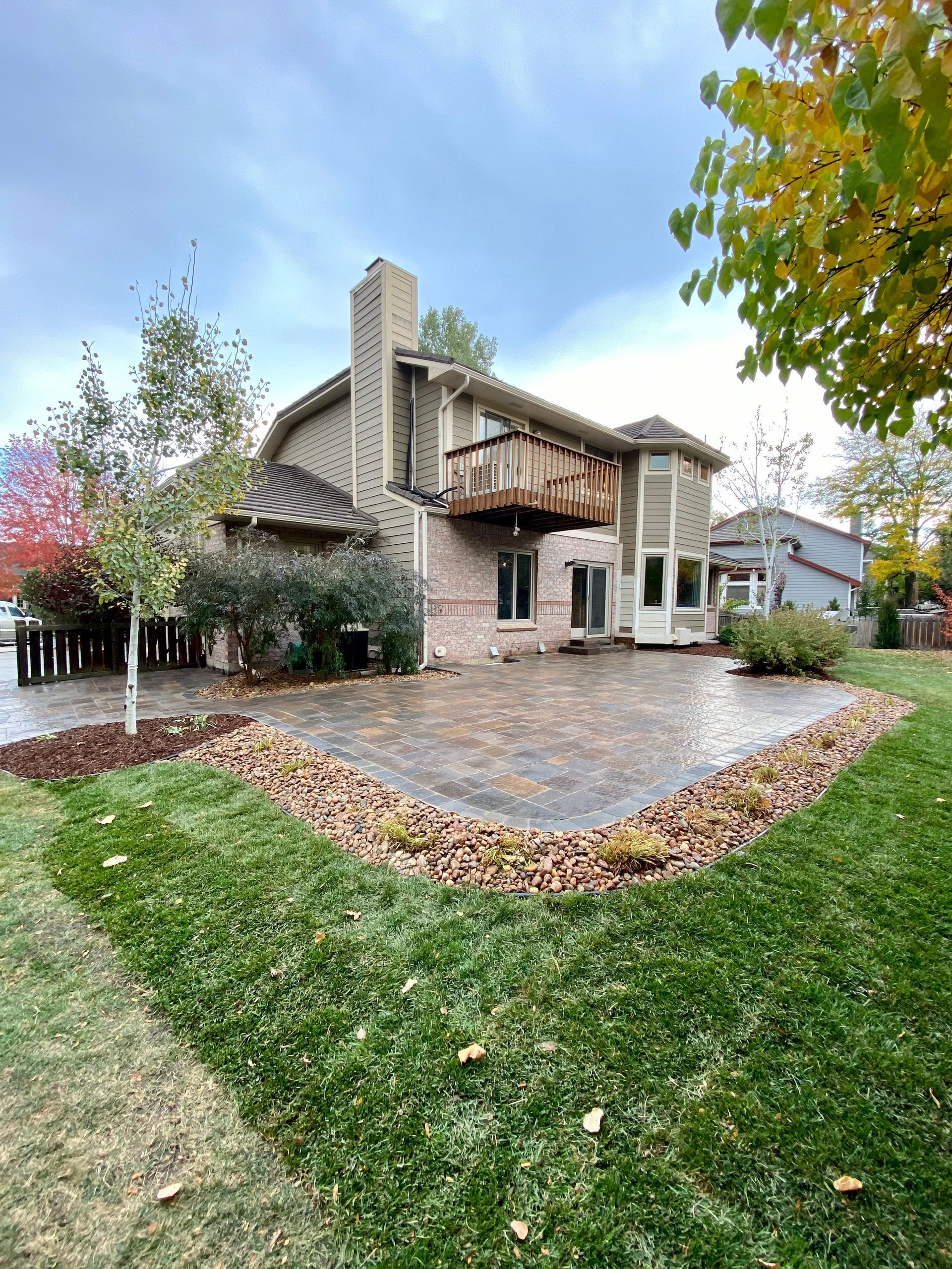 Backyard patio with a brick house, green grass, and colorful autumn trees.