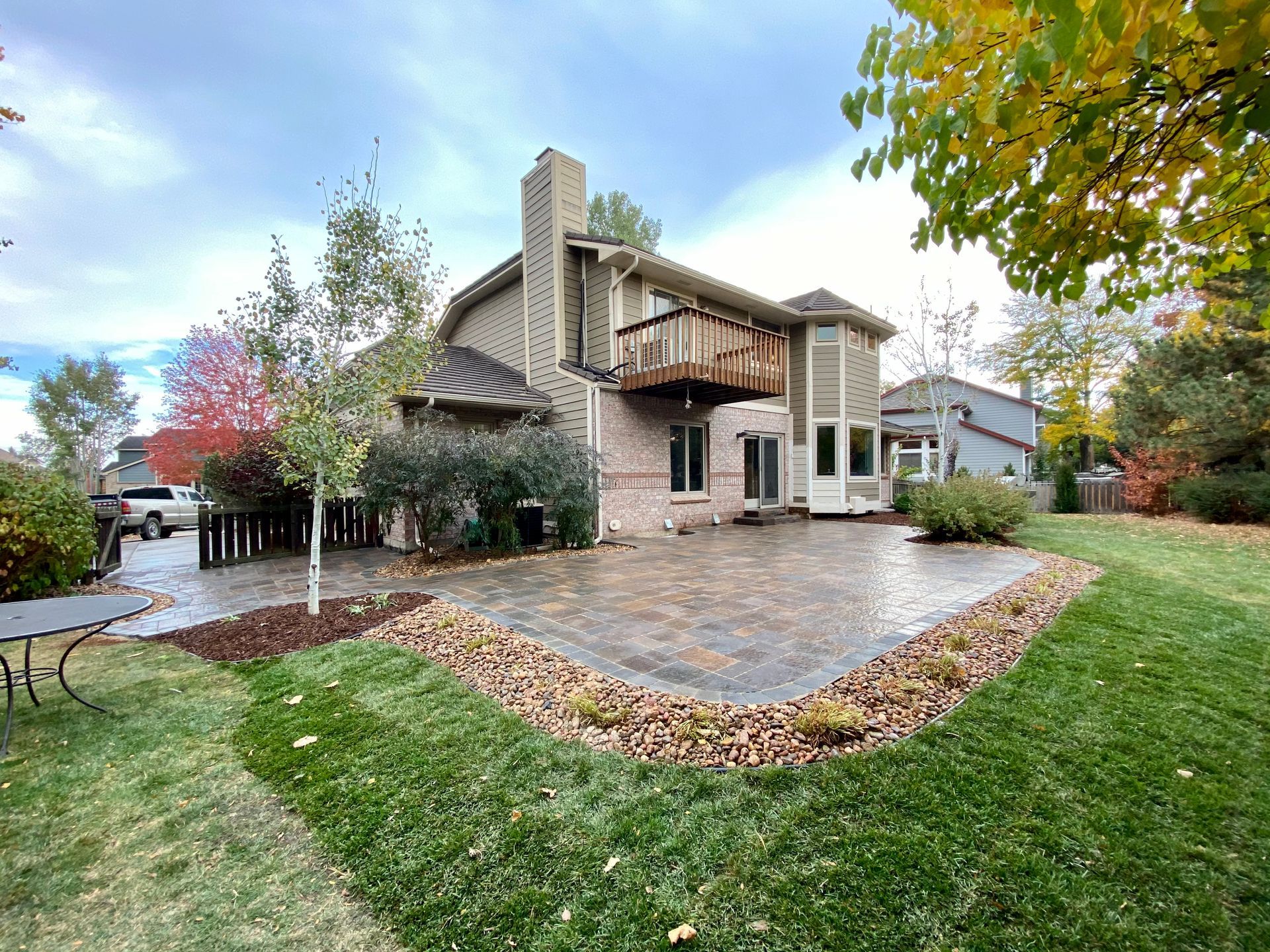 Backyard with brick house, patio, and landscaping in fall colors.