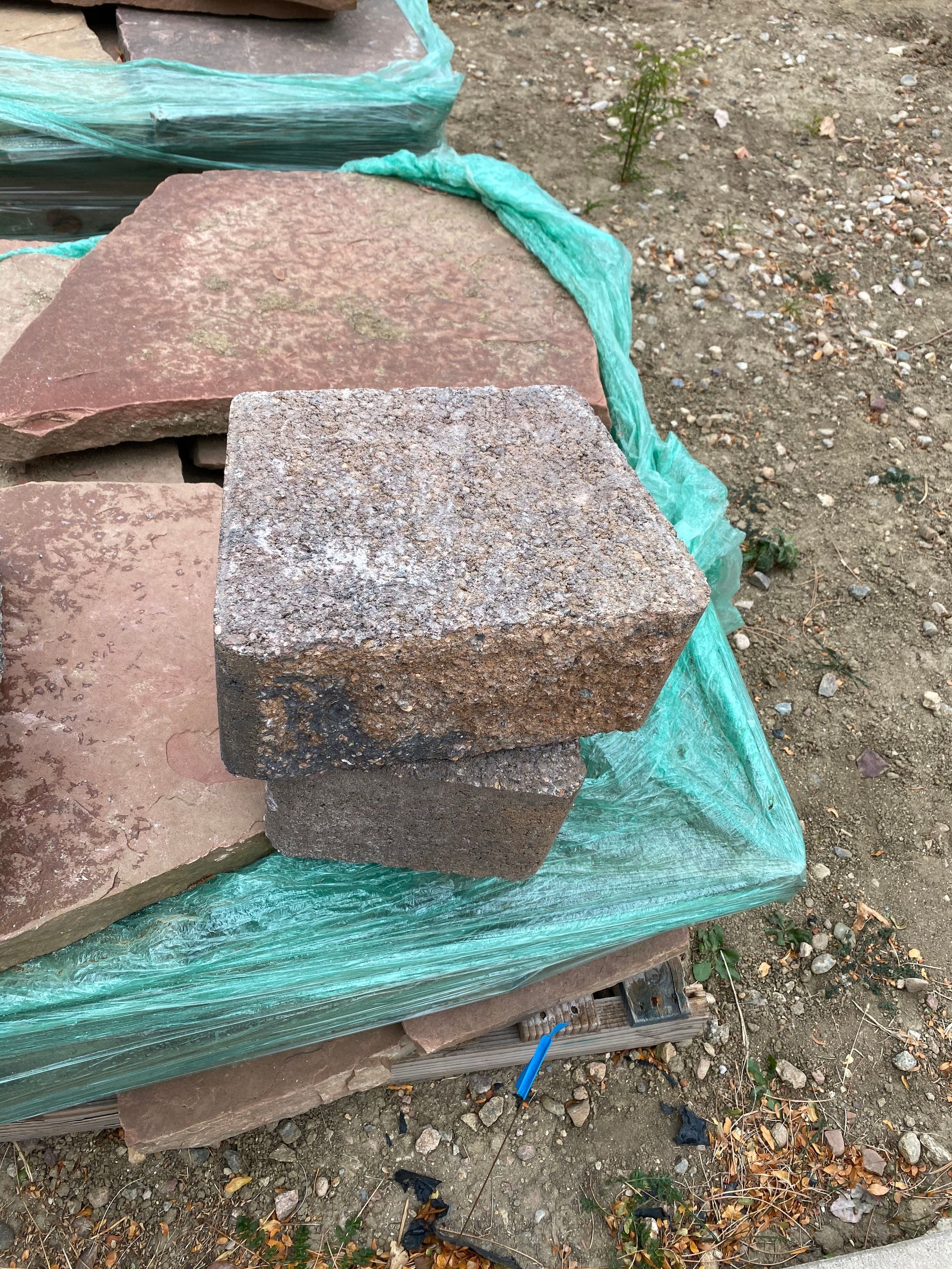 Stack of brown and grey paving stones wrapped in green netting, outdoors.