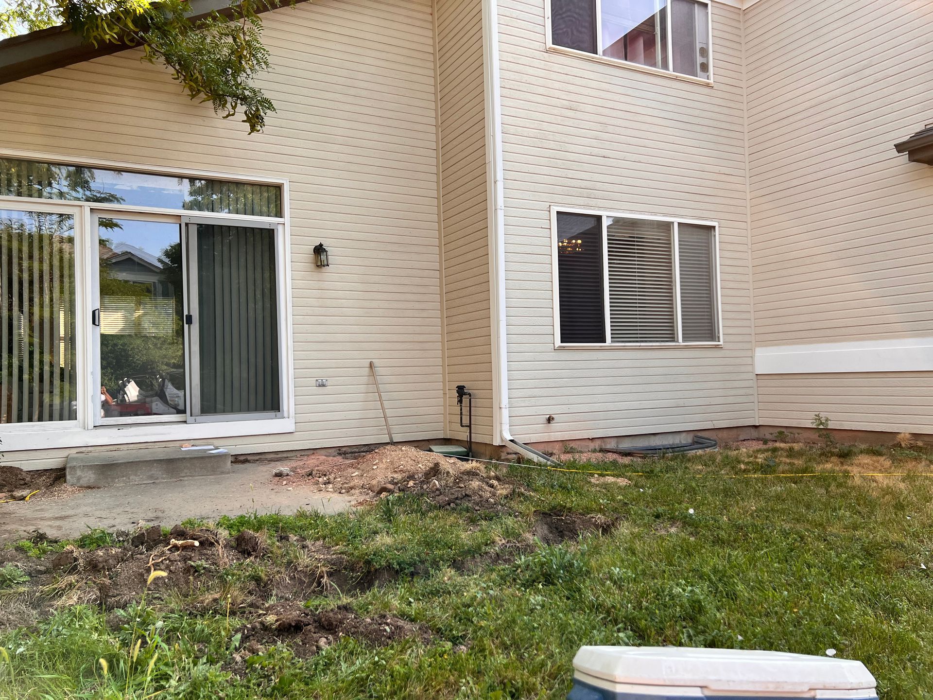 Beige house exterior with sliding glass doors, windows, and patchy lawn.