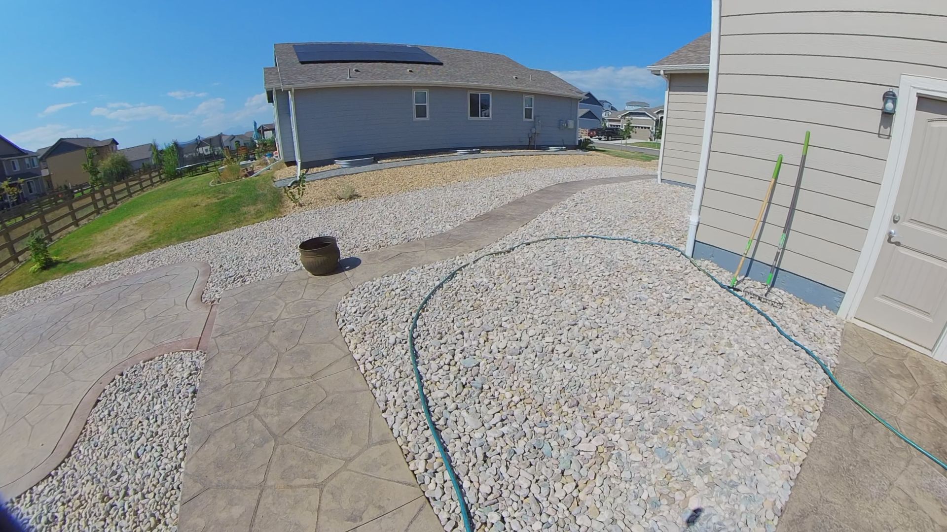 A house with solar panels, a rock path, and a hose on a sunny day.