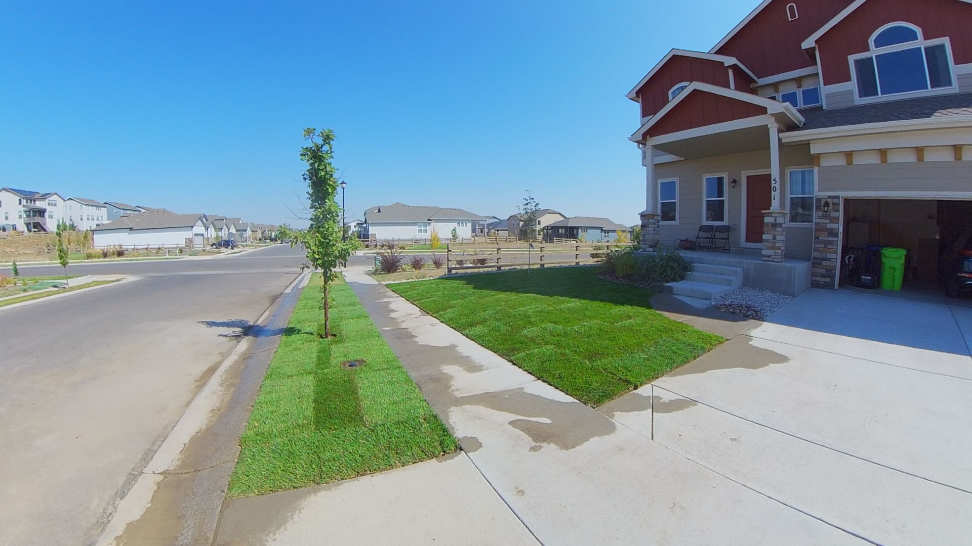 A two-story house with red accents, a green lawn, and a sidewalk on a sunny day.