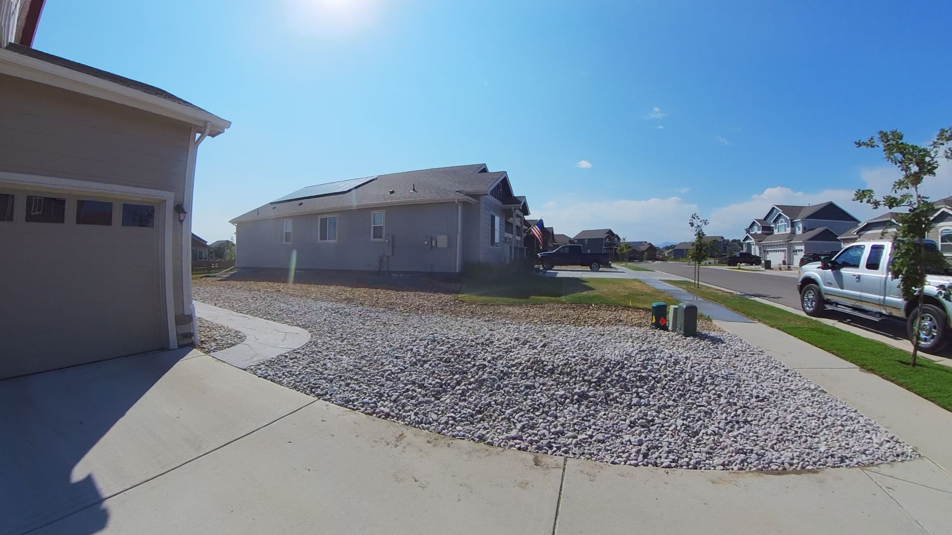Exterior of house with garage, gravel landscaping, blue sky, and parked truck on the street.