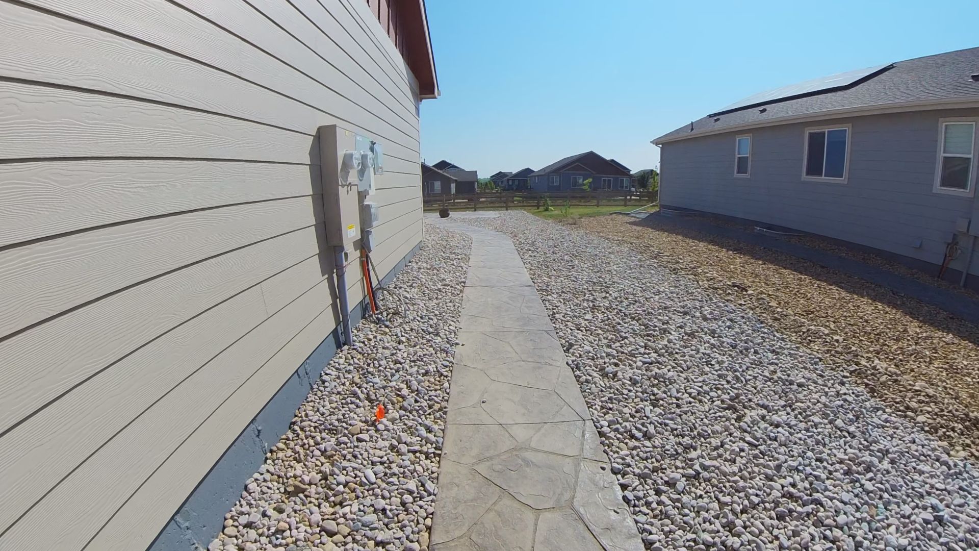 Stone path between houses with gravel and clear sky.