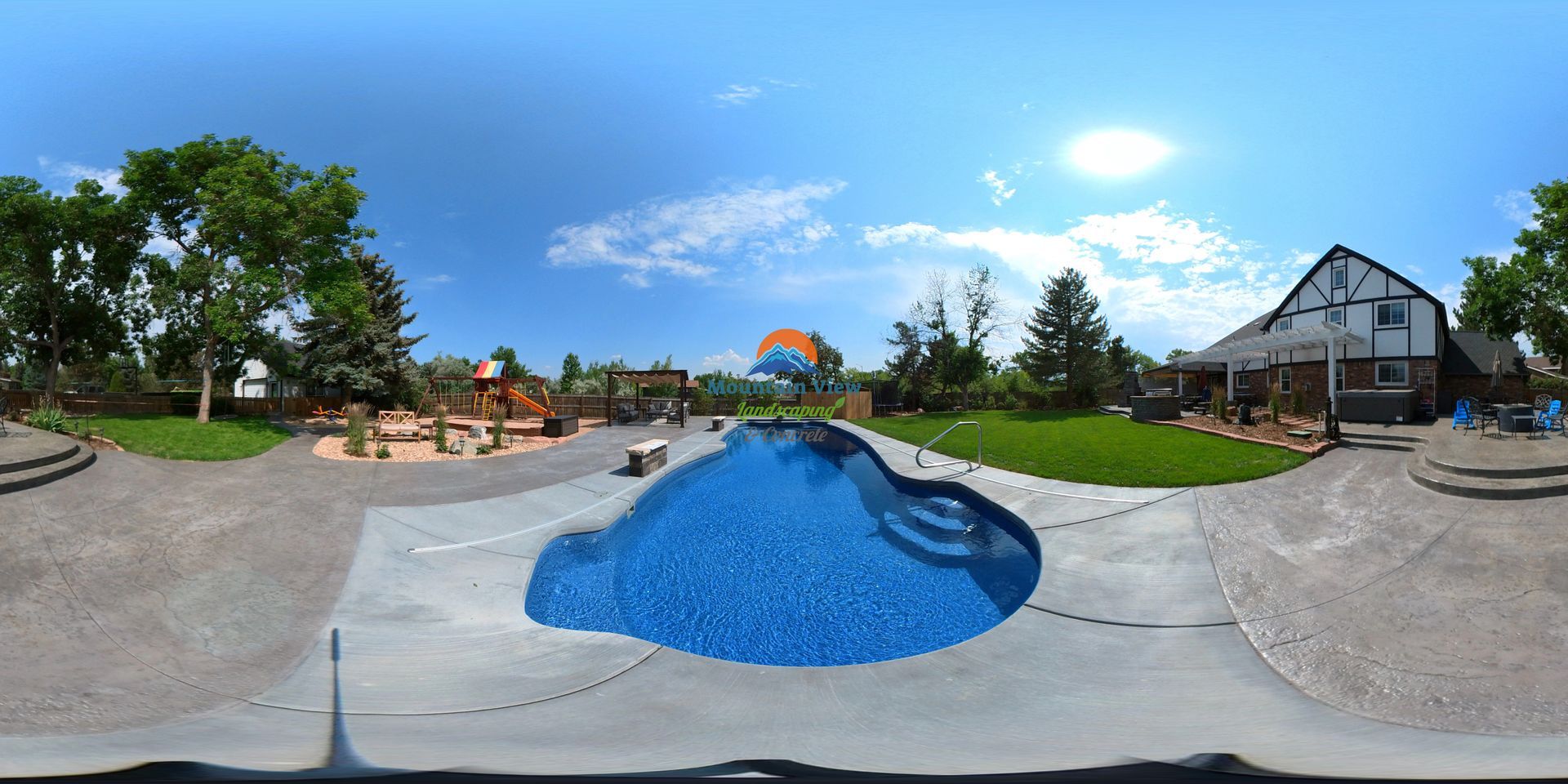 A backyard with a pool, playground, and large house on a sunny day.