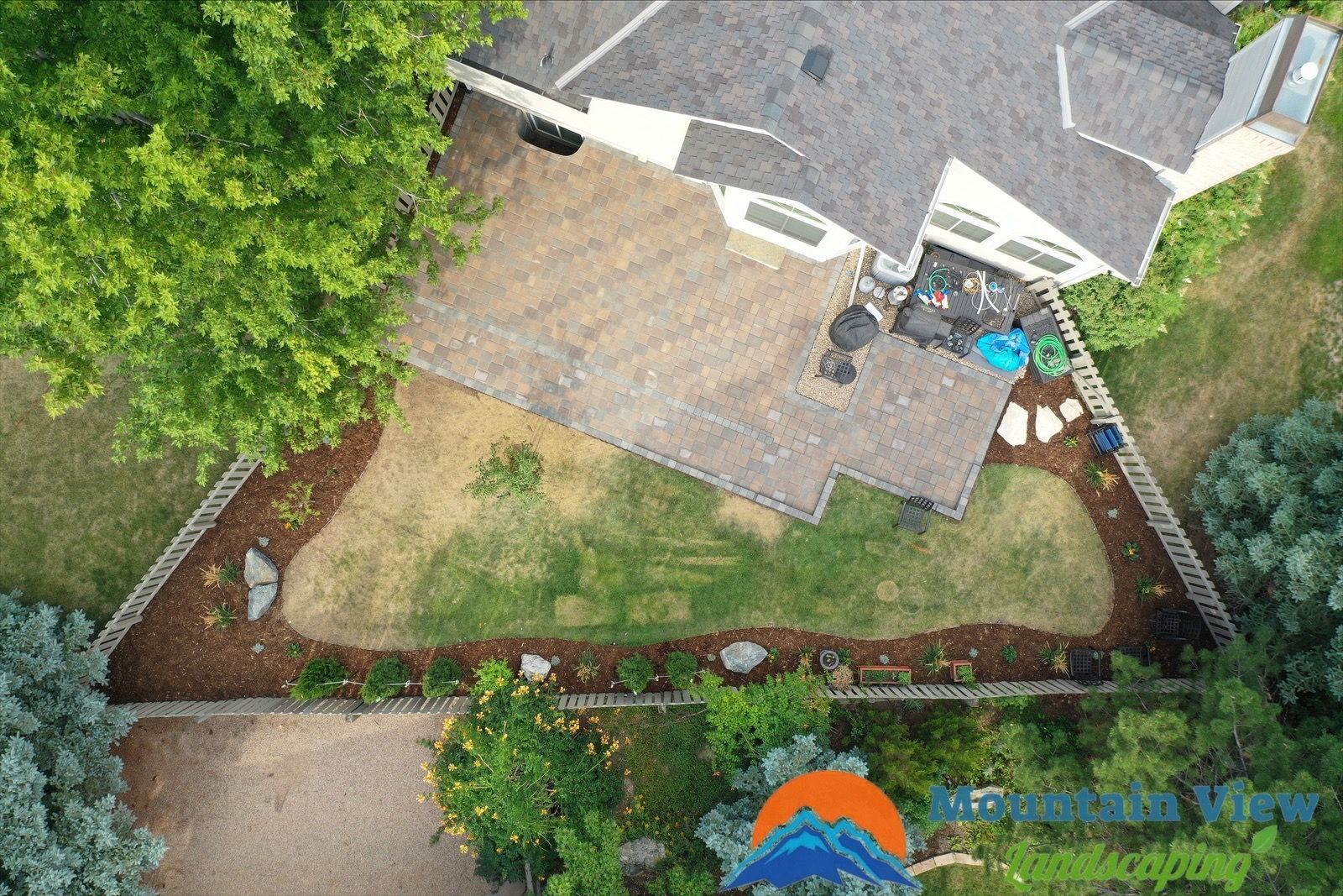 Aerial view of a house with a backyard garden, patio, and lawn surrounded by trees and decorative landscaping.