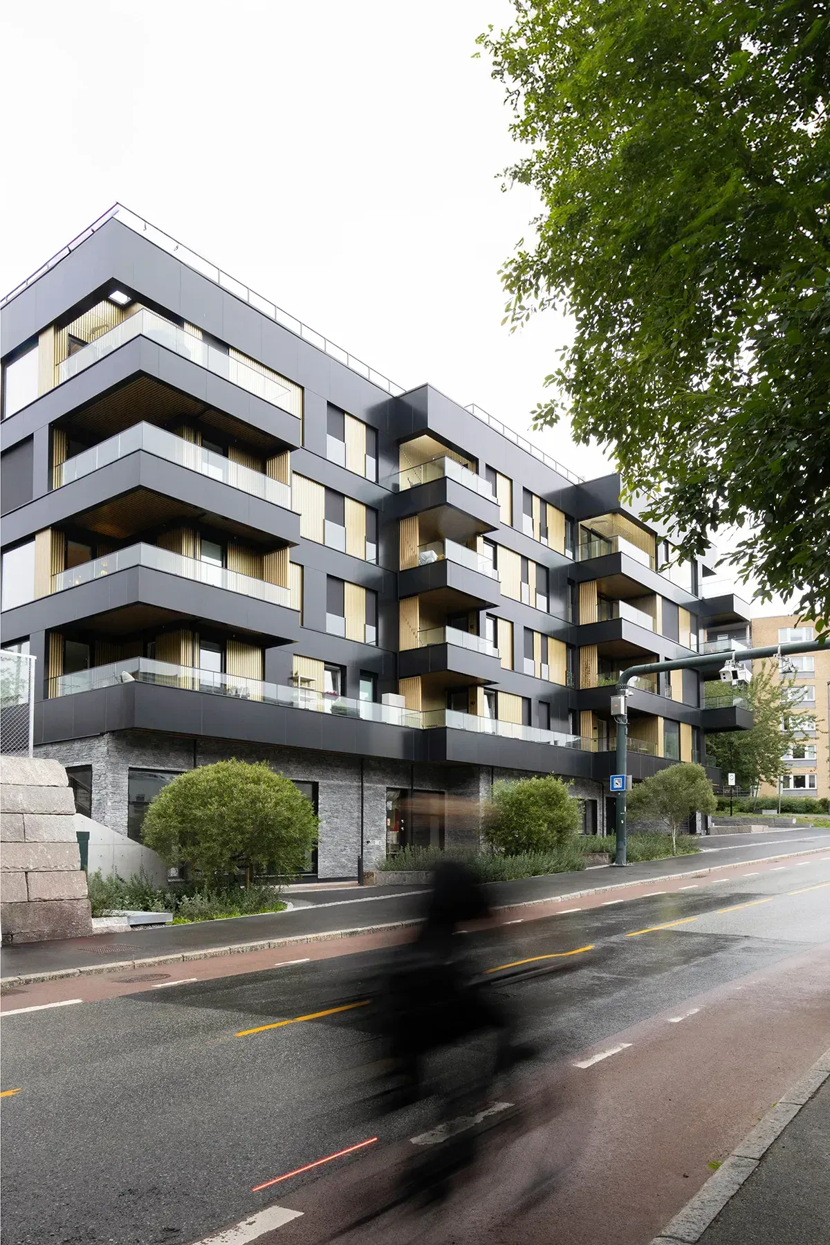 Boligbygg på Tøyentaket sett fra Ensjøveien med fasaderytme, mørk sokkel, gule og svarte plater og glassbalkonger