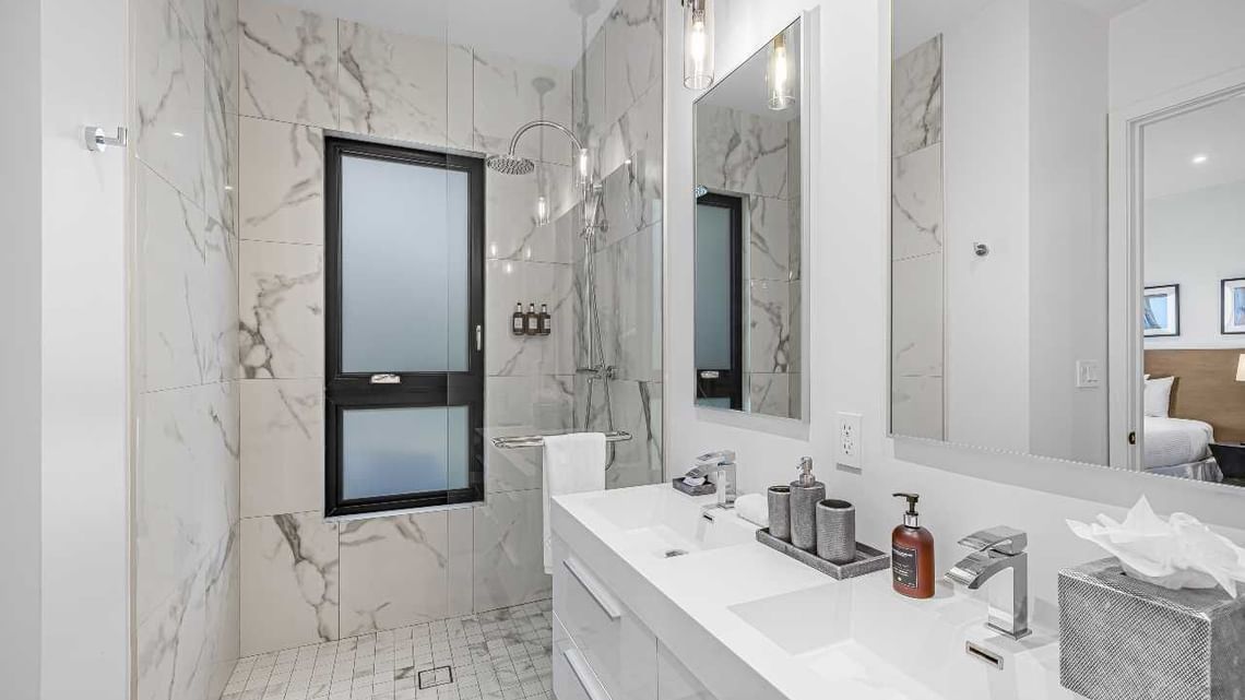 Modern white bathroom with marble walls, double vanity, large mirror, and glass shower window