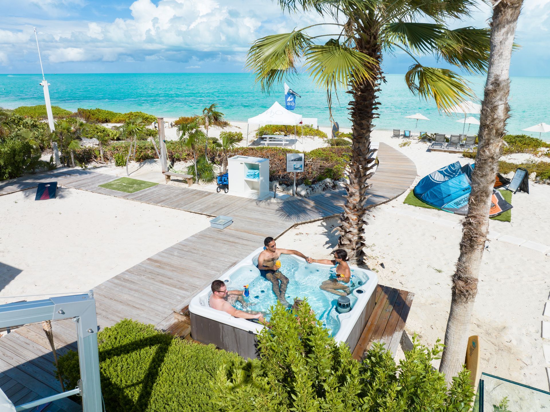Beachside pool area with people relaxing in a hot tub near palm trees and turquoise water