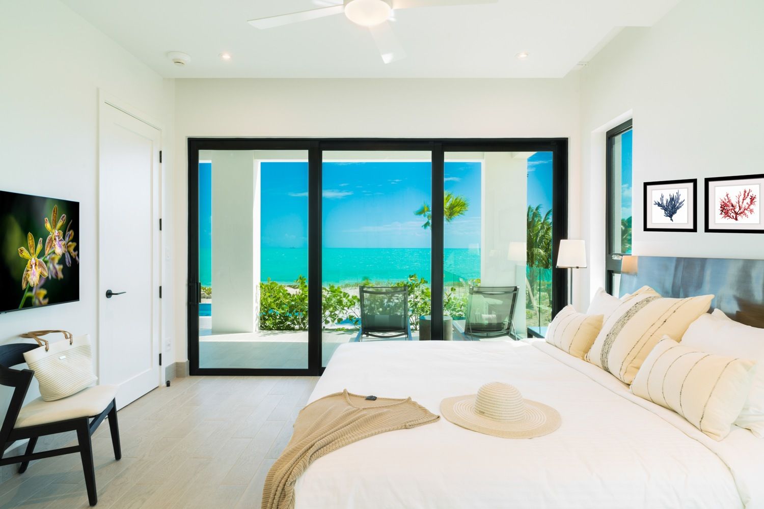 Bright bedroom with ocean view, black-framed glass doors, white bedding, and turquoise sea beyond the balcony