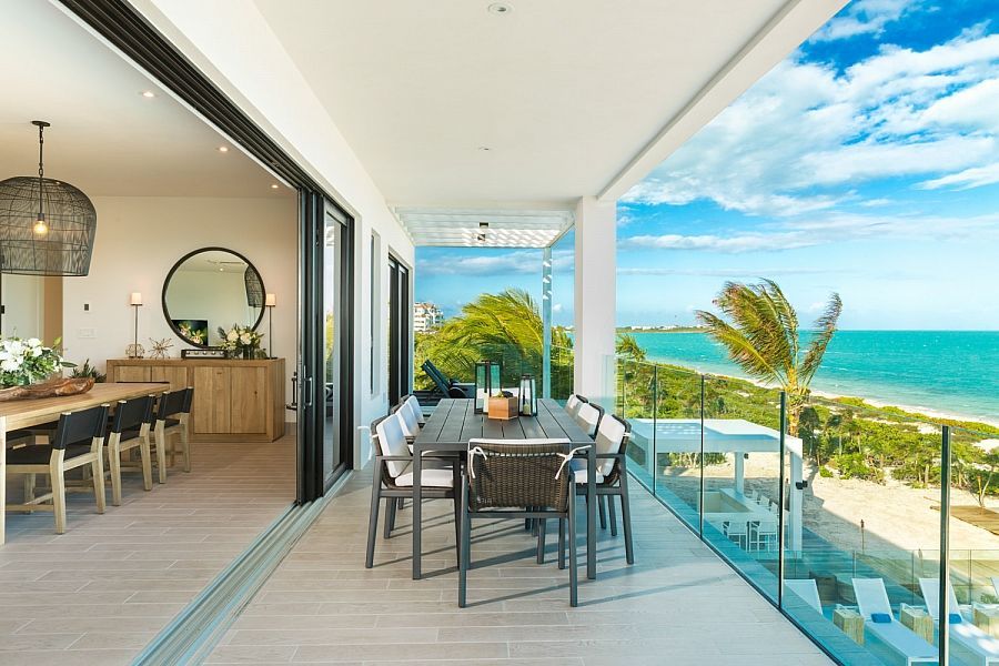 Modern oceanfront balcony with dining table, glass railing, and turquoise sea view