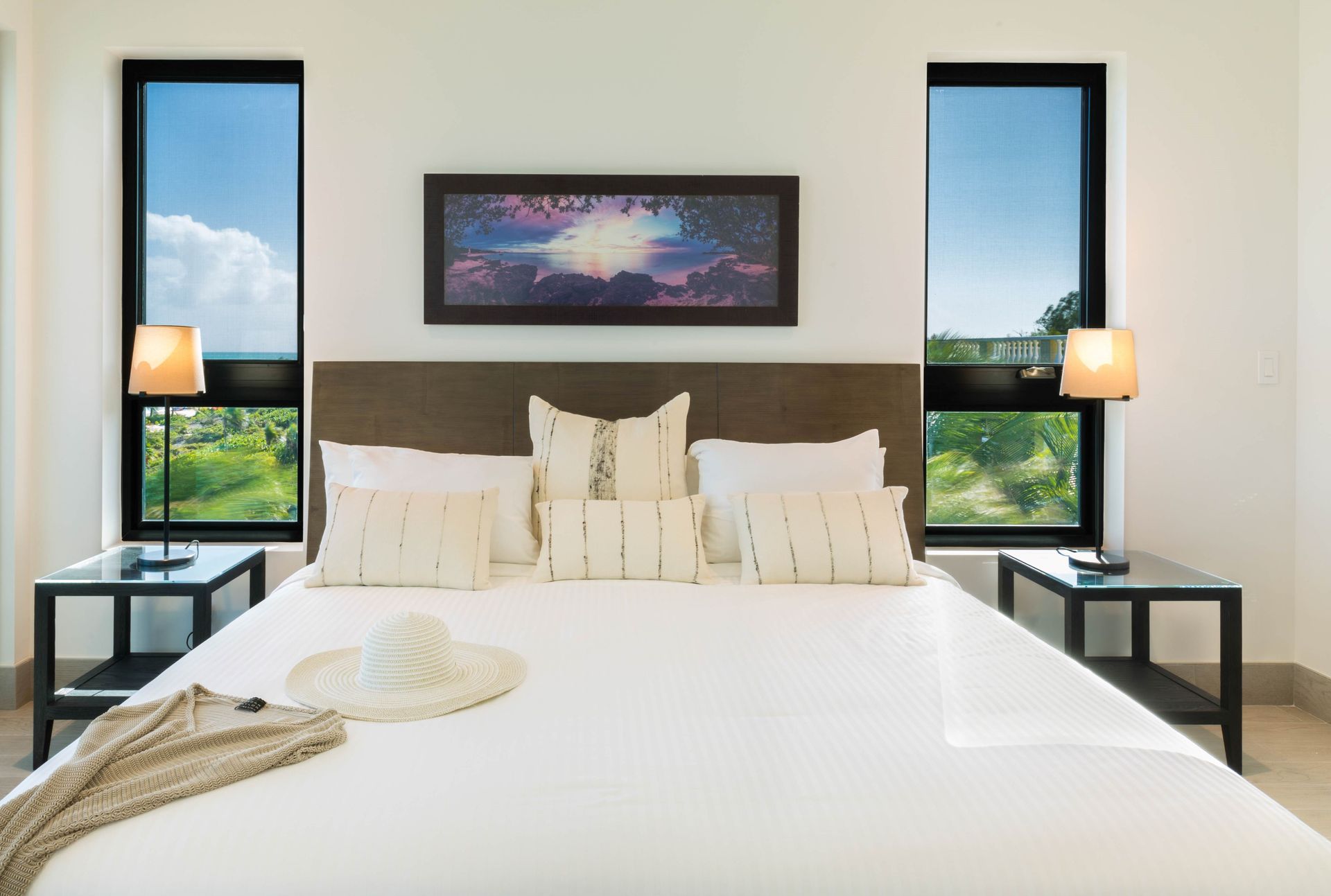 Bright bedroom with a king bed, white bedding, bedside lamps, and windows on both sides.