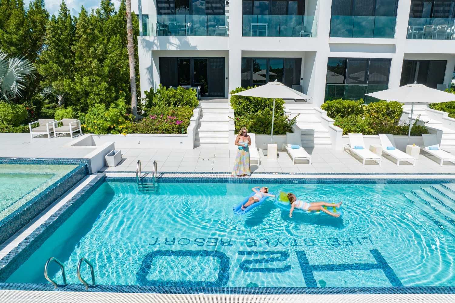 Modern pool with swimmers and lounge chairs outside a glass-fronted building