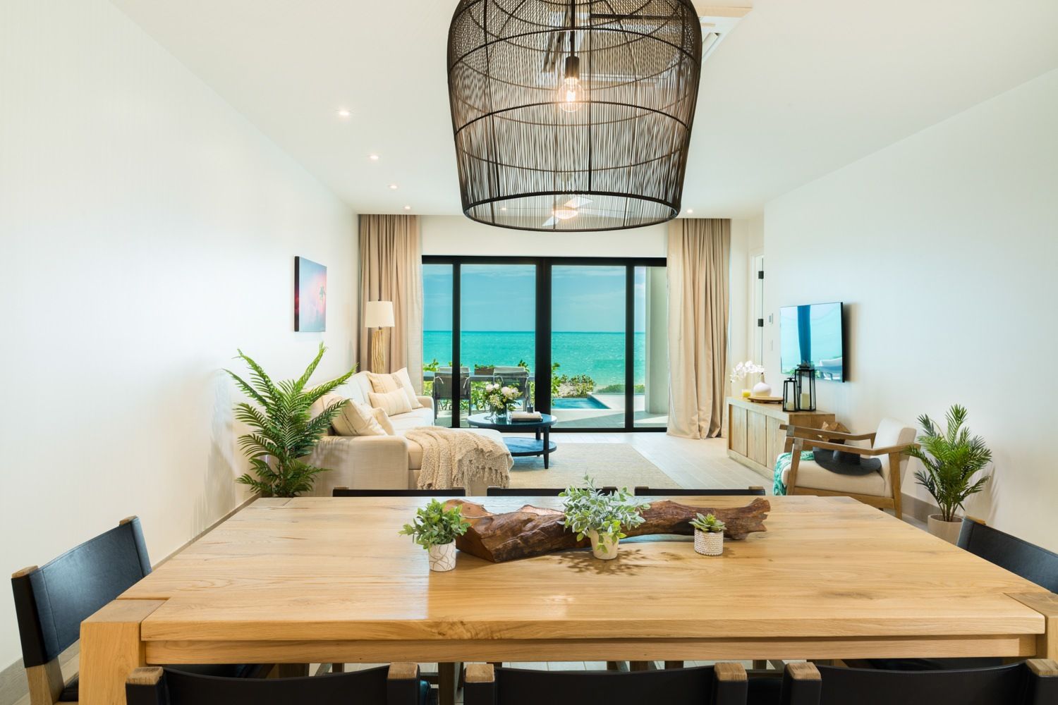 Bright modern dining-living room with wood table, white sofa, and ocean view through sliding glass doors
