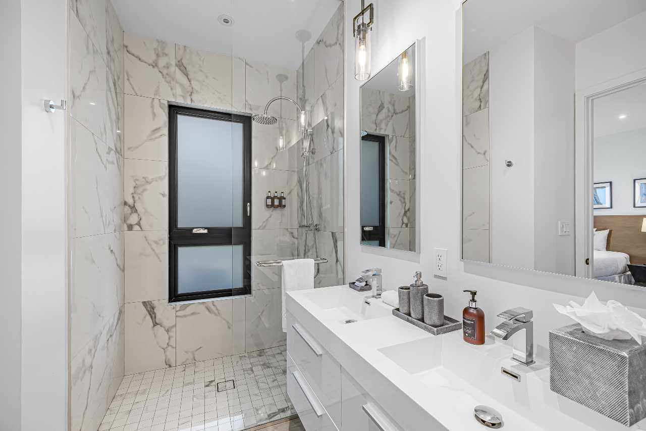 Modern white bathroom with marble walls, double vanity, large mirror, and walk-in shower.