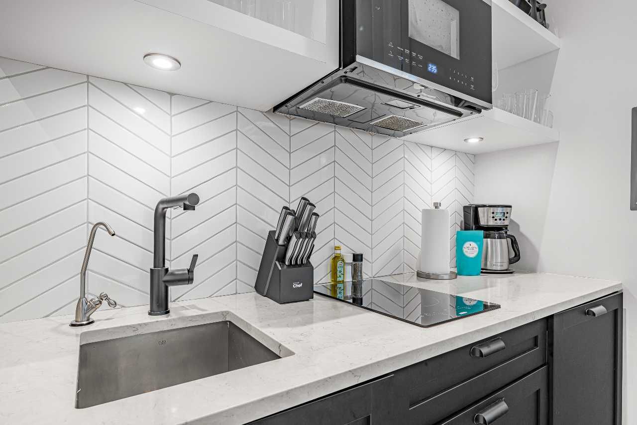 Modern white kitchen counter with sink, black faucet, chevron backsplash, microwave, and coffee maker