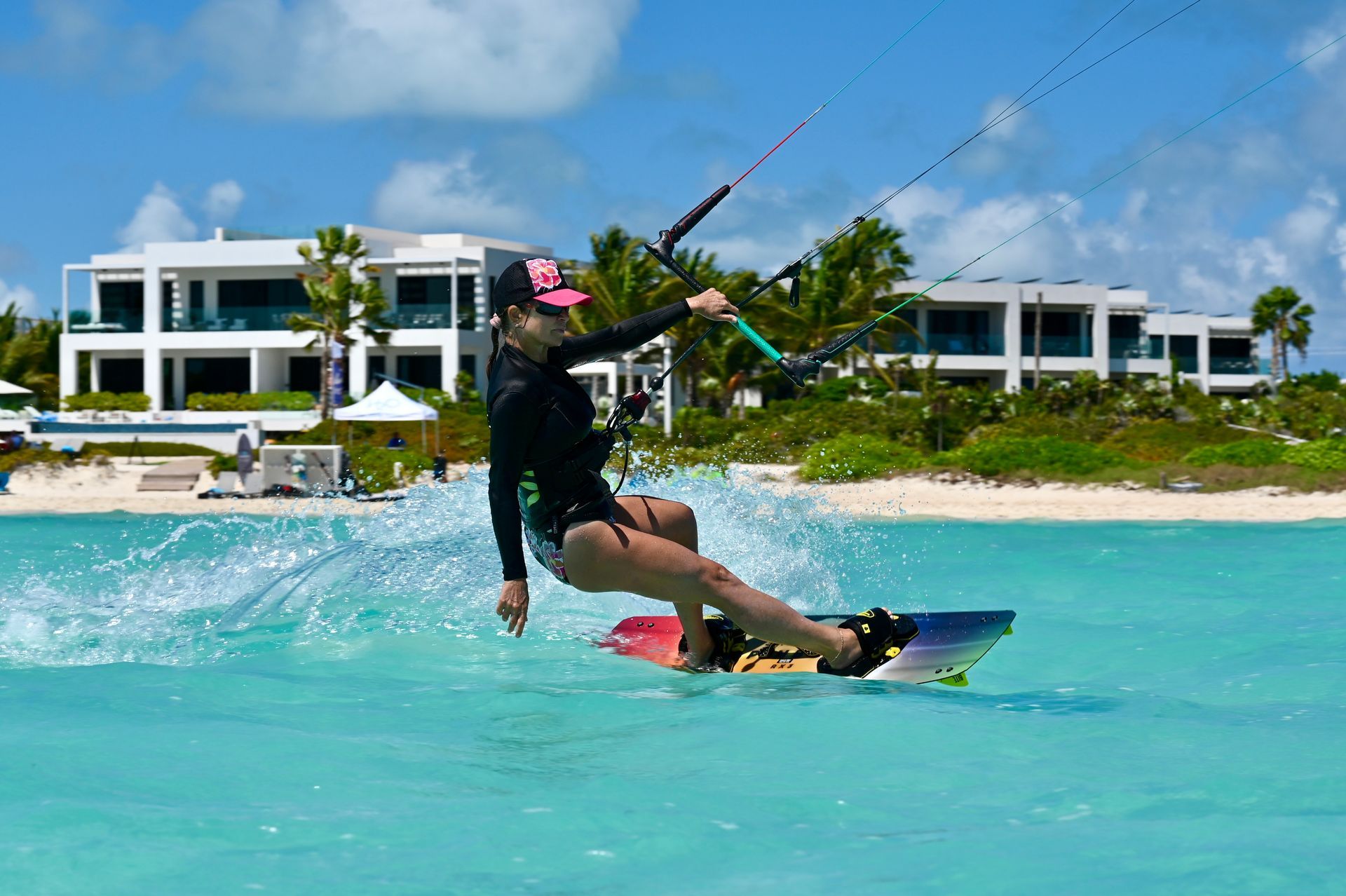 Kiteboarder gliding across turquoise water in front of beachfront resort buildings