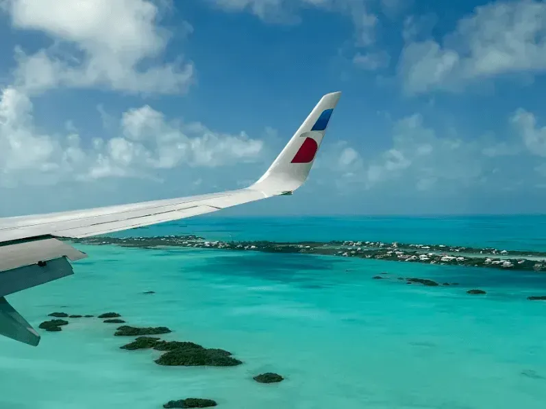 Airplane wing over turquoise tropical water and small islands under a partly cloudy sky