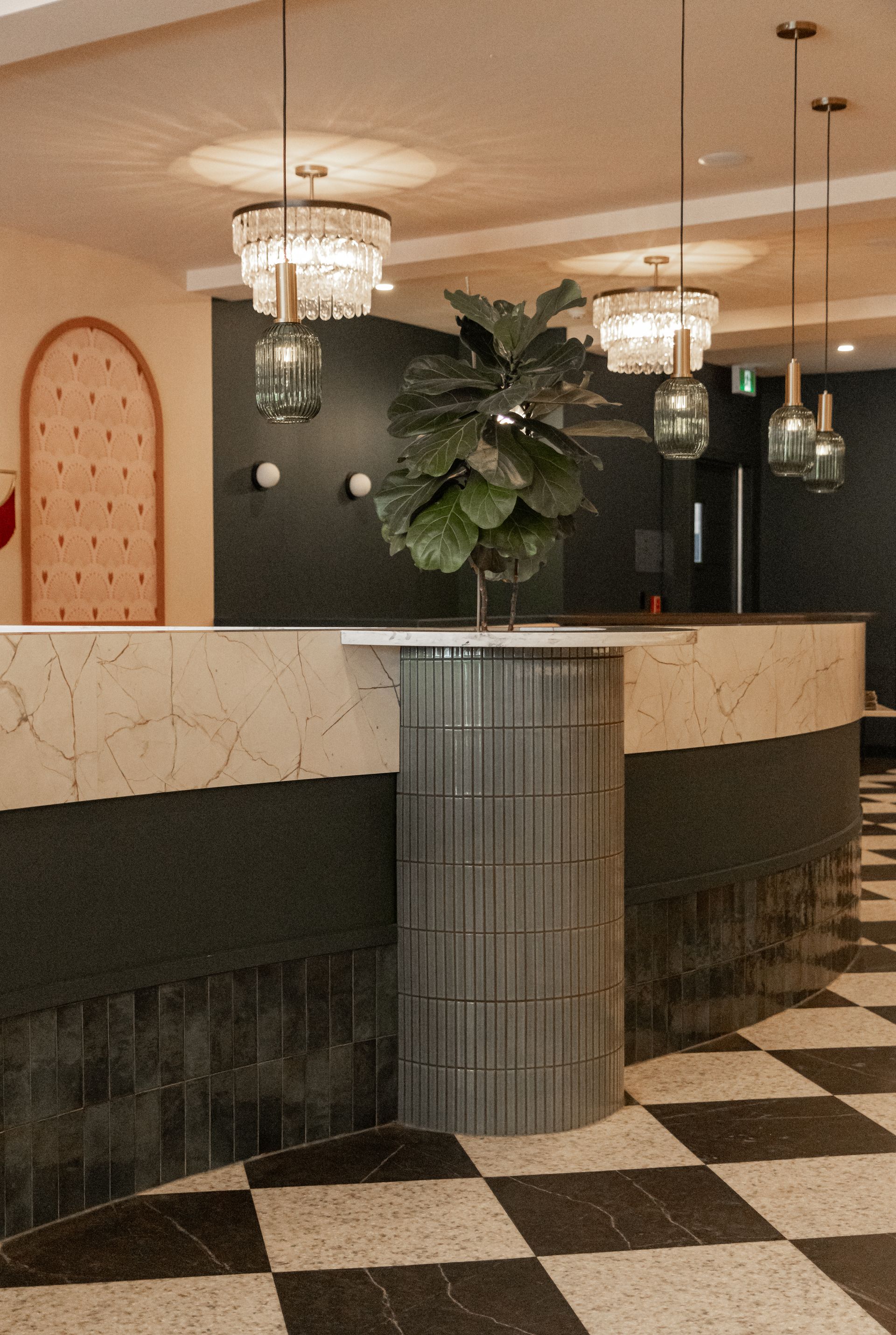 Élégant comptoir de réception d'hôtel avec lustres, mur sombre et sol à damier noir et blanc.