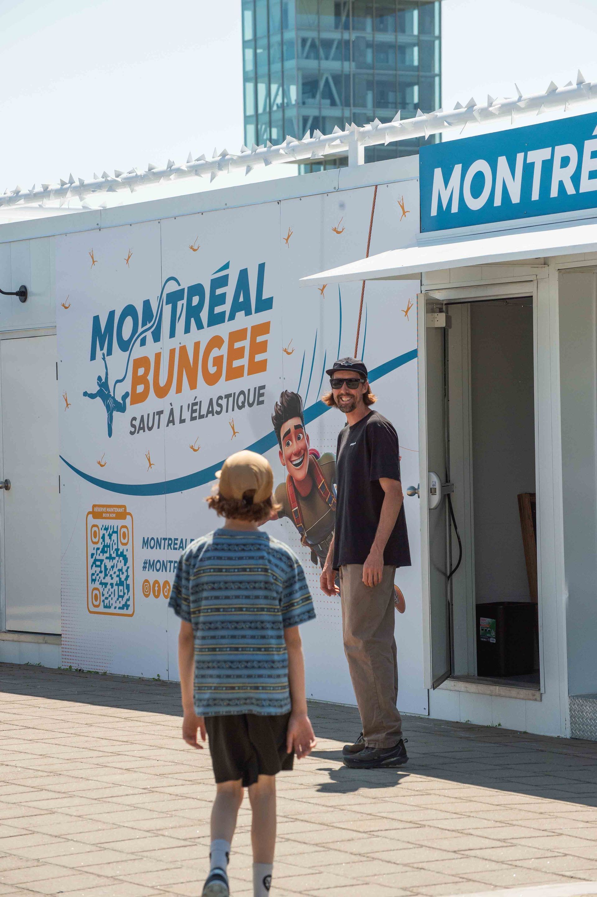 Des personnes se tiennent devant l'attraction de saut à l'élastique de Montréal, à côté d'un bâtiment blanc avec une enseigne bleue.