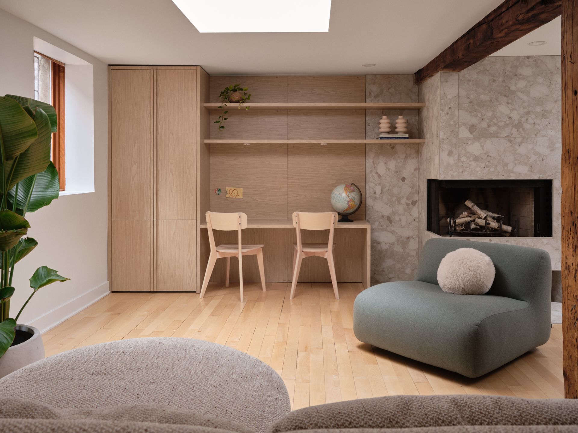 Bureau à domicile moderne avec rangements intégrés en bois clair, bureau, deux chaises, cheminée et canapé vert.