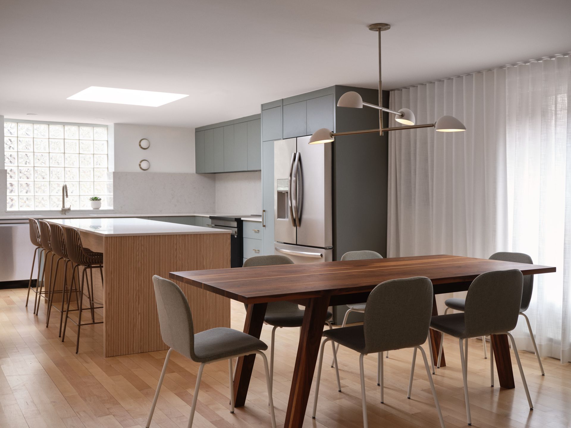 Cuisine et salle à manger modernes avec parquet, îlot central avec tabourets de bar et table à manger avec chaises.