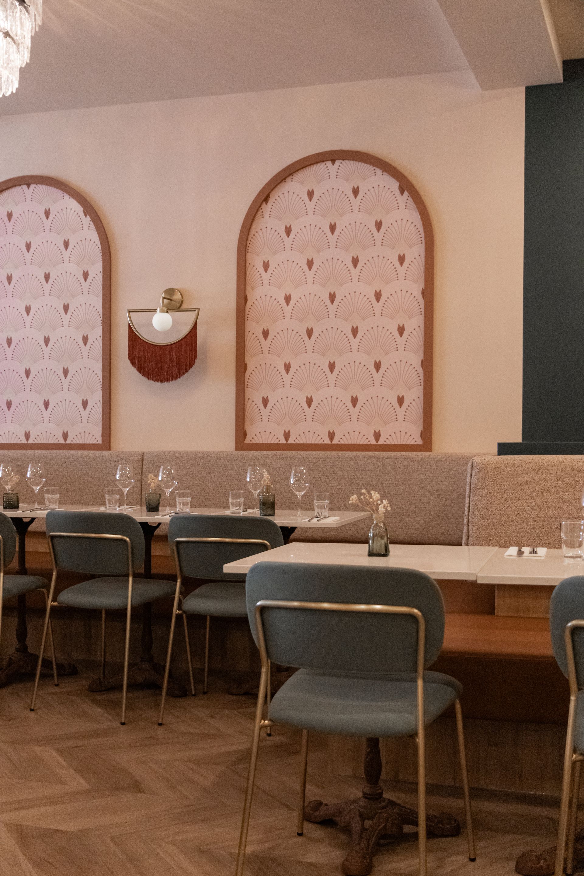 Intérieur de café cosy avec des panneaux muraux arqués roses, des tables en bois et des chaises vertes le long d'un comptoir carrelé.