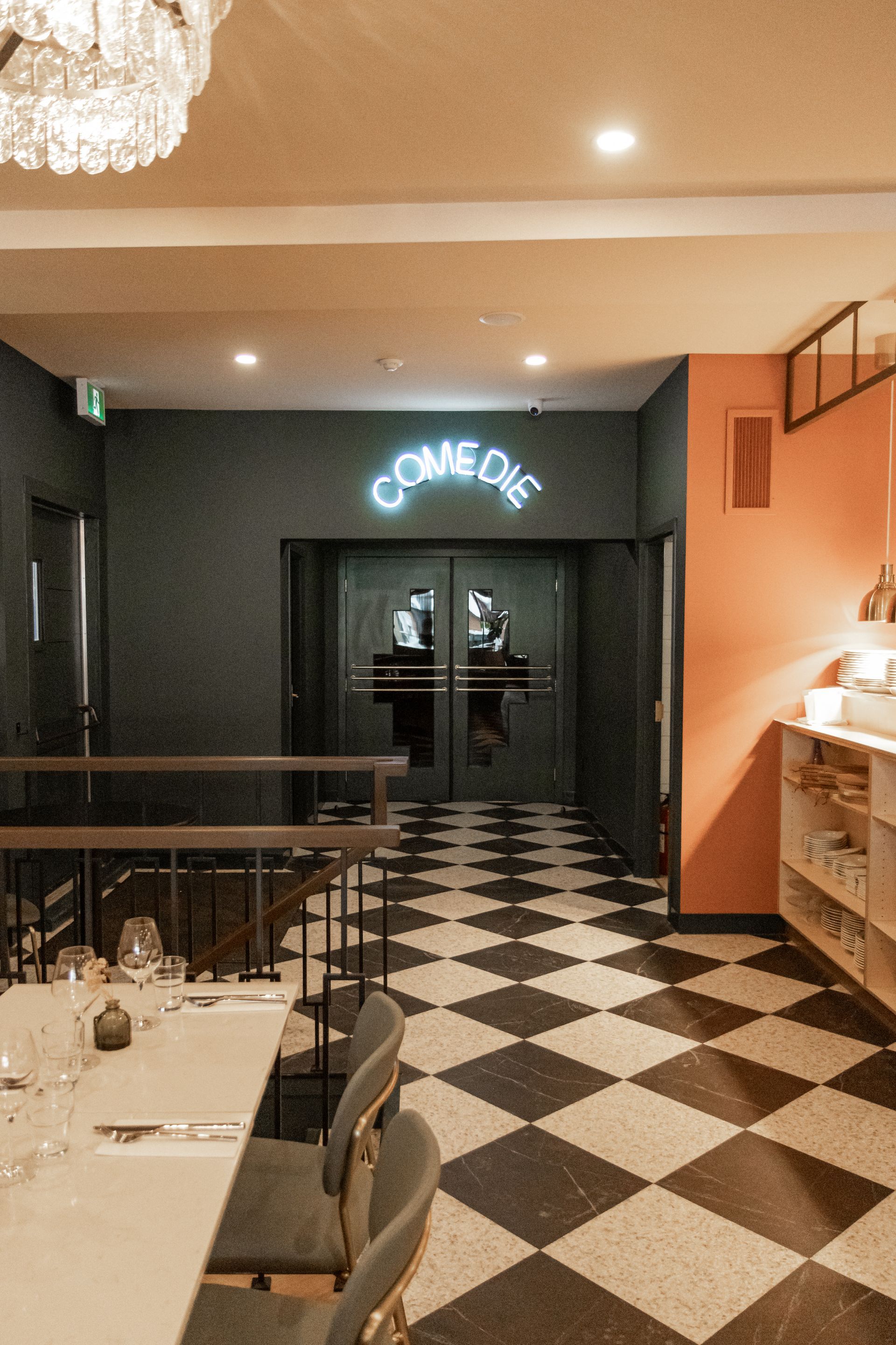 Intérieur tamisé du restaurant, sol à damier noir et blanc et enseigne lumineuse « COME ON » au-dessus des portes doubles