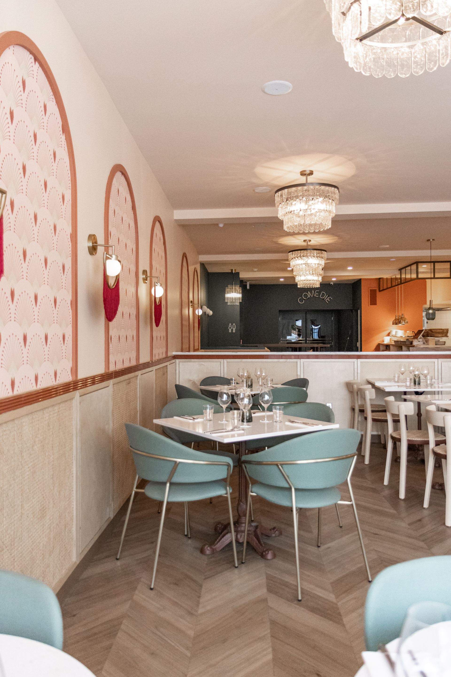 Intérieur élégant d'un café aux tons pastel, avec chaises turquoise, tables en marbre, sol à motifs et luminaires suspendus chaleureux.