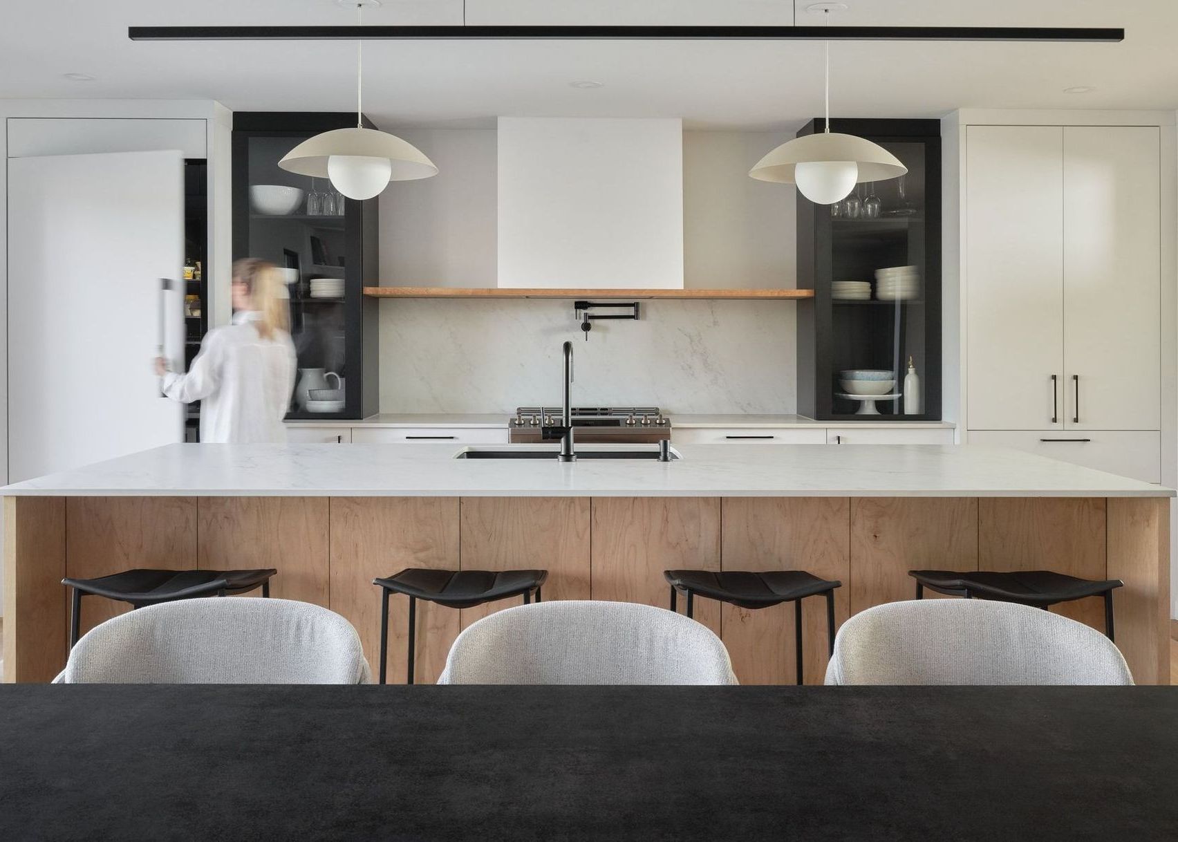 Cuisine moderne avec comptoirs blancs et îlot en bois, garde-manger à ouverture latérale.