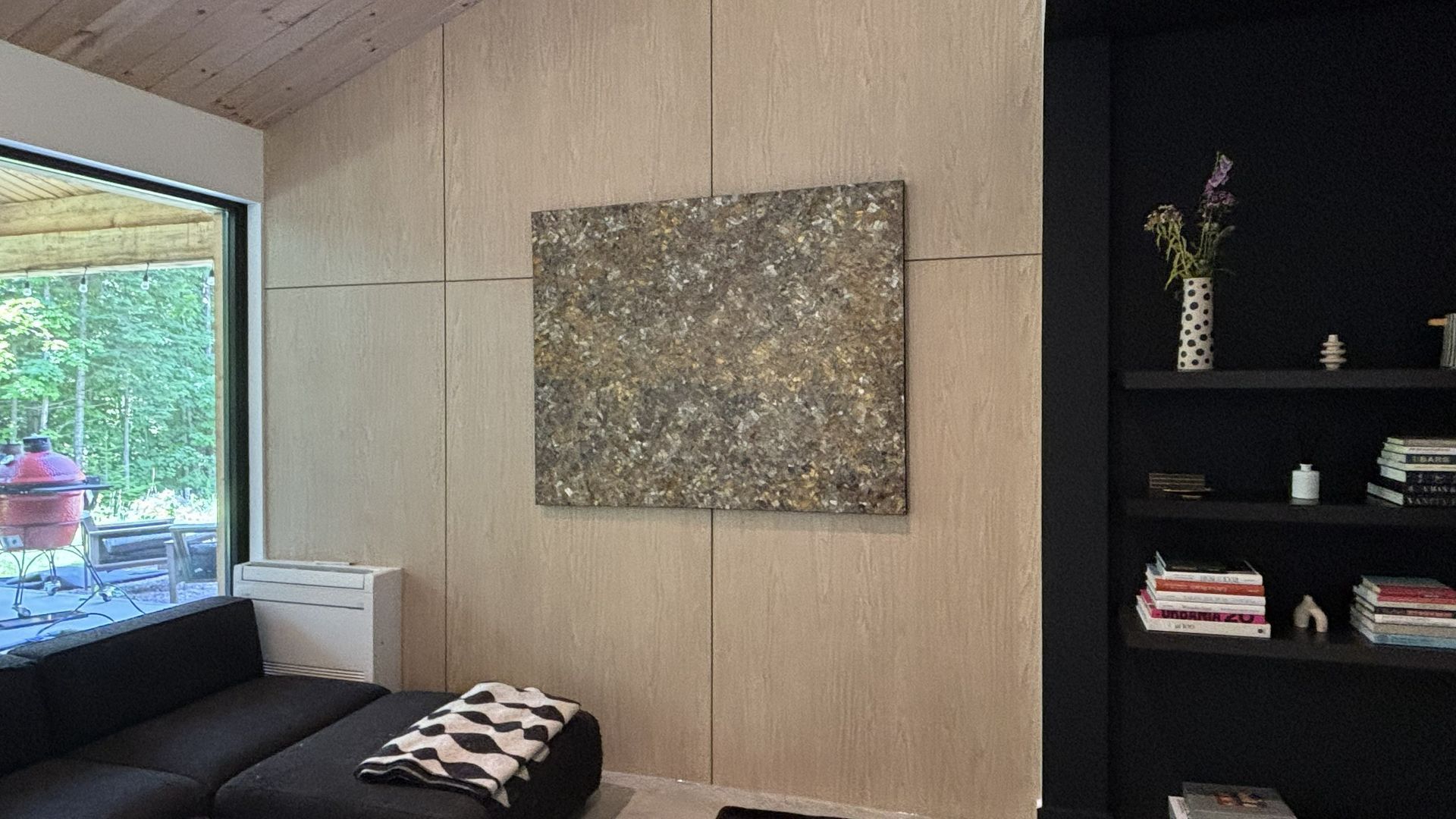 Salon moderne avec grande fenêtre, canapé noir, tableau beige et étagère noire