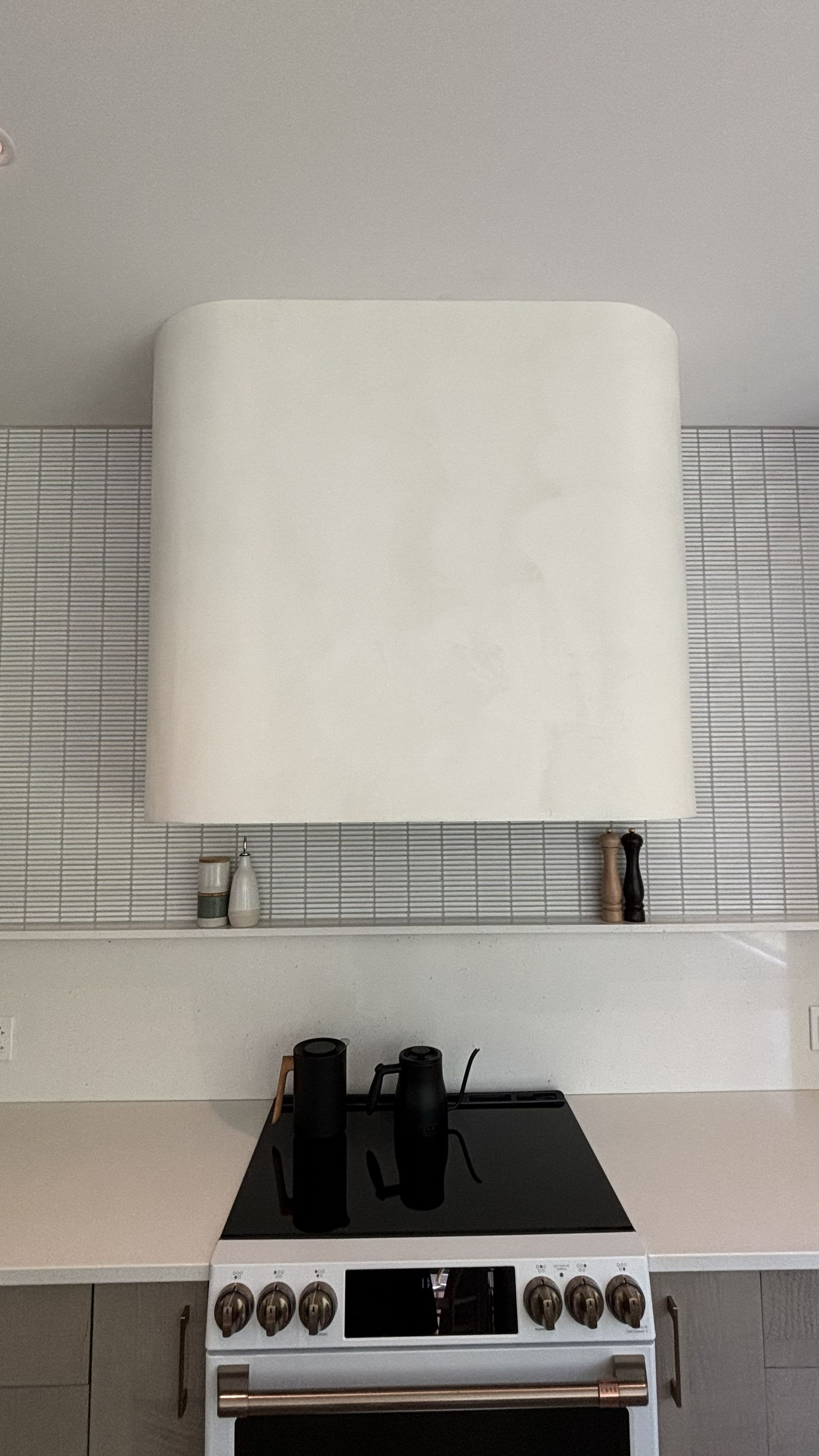 Petite cuisine avec une hotte blanche au-dessus d'une cuisinière et des appareils électroménagers noirs sur le plan de travail.