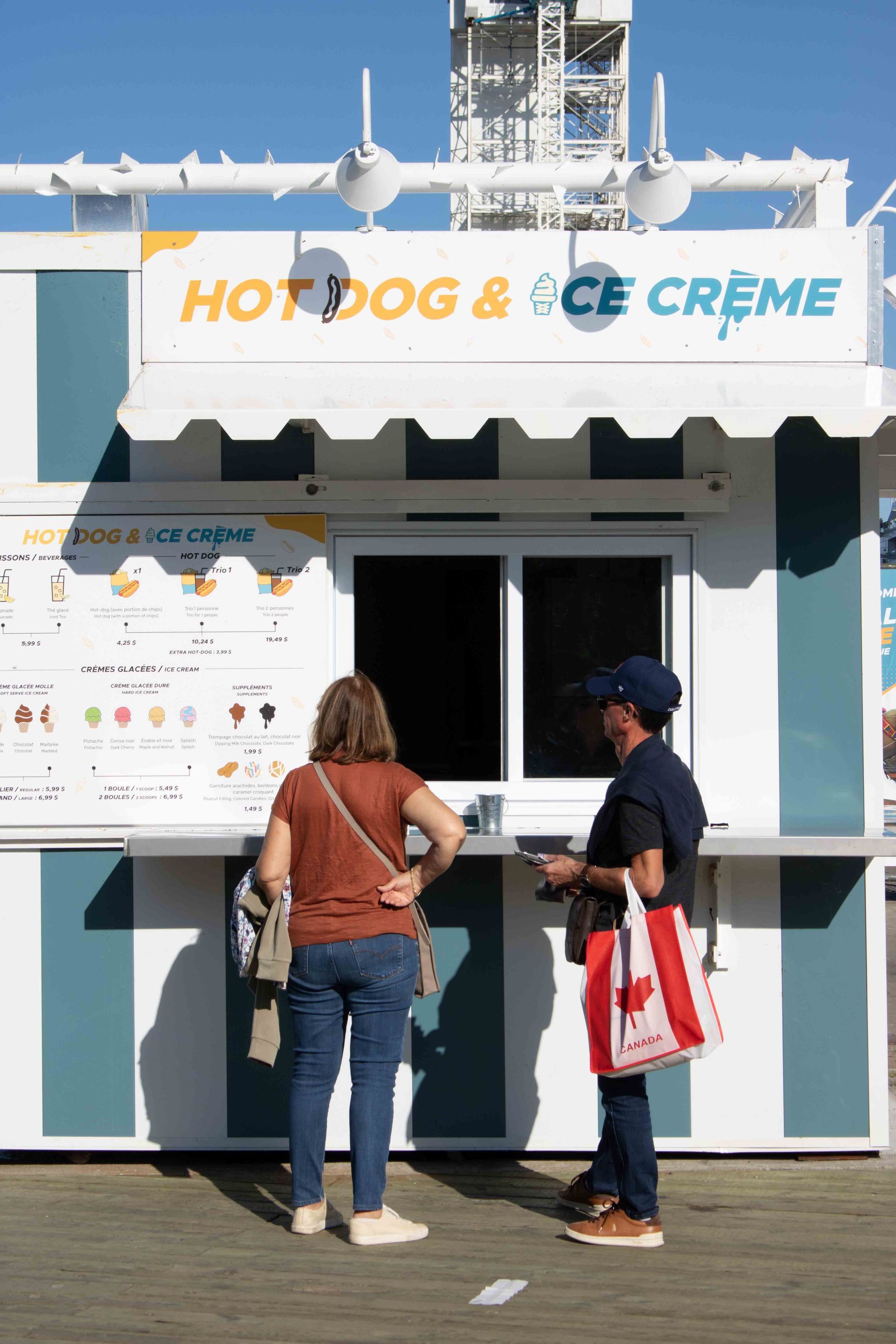 Deux personnes commandent des hot-dogs blancs et des glaces à un stand situé sur une promenade.