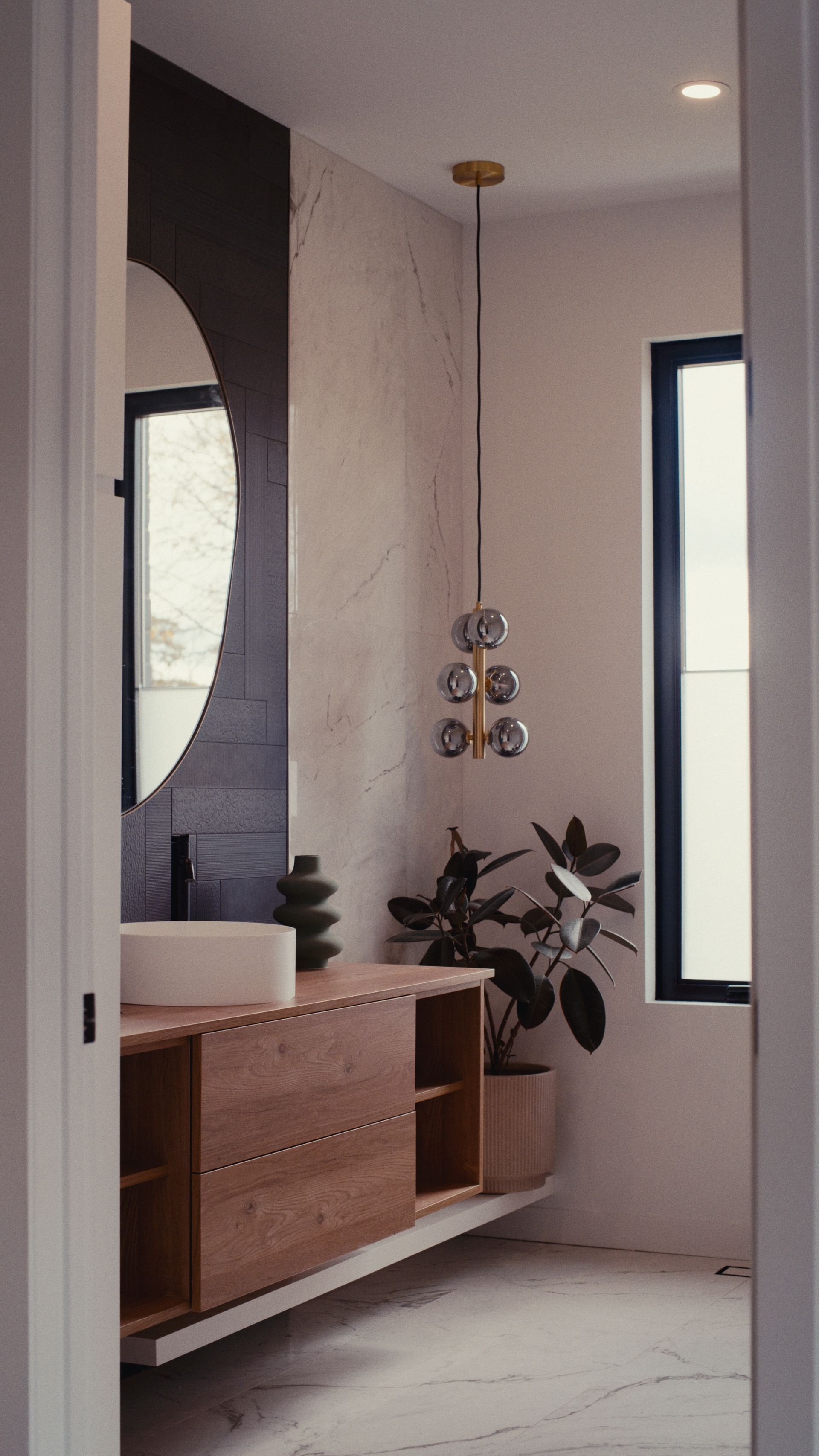 Salle de bains avec meuble-lavabo en bois, miroir rond, suspension lumineuse et plante en pot.