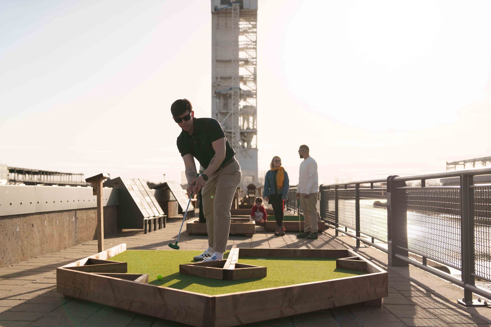 Une personne jouant au mini-golf près d'une rambarde au coucher du soleil